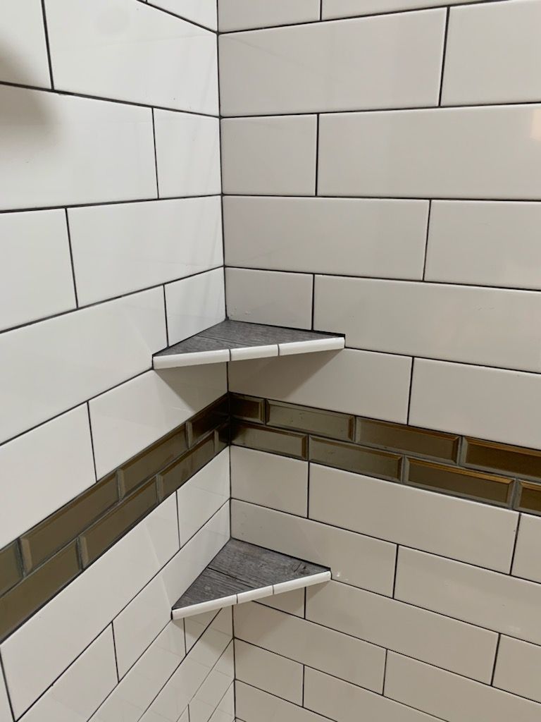 Corner of a tiled shower with two small triangular corner shelves and a brown accent tile band