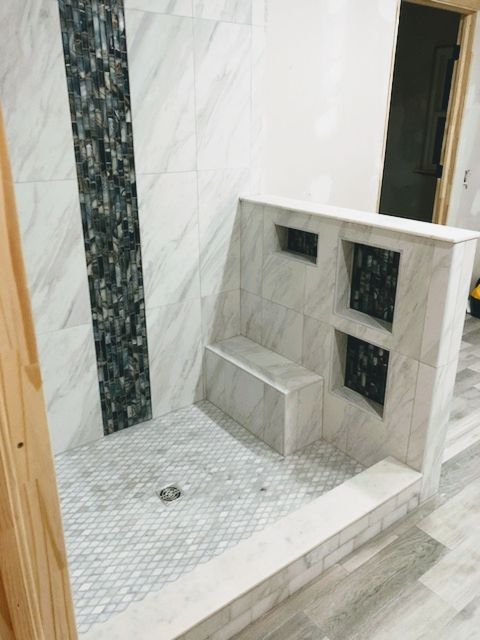 Marble-tiled shower with a built-in bench, mosaic floor, and dark accent niches