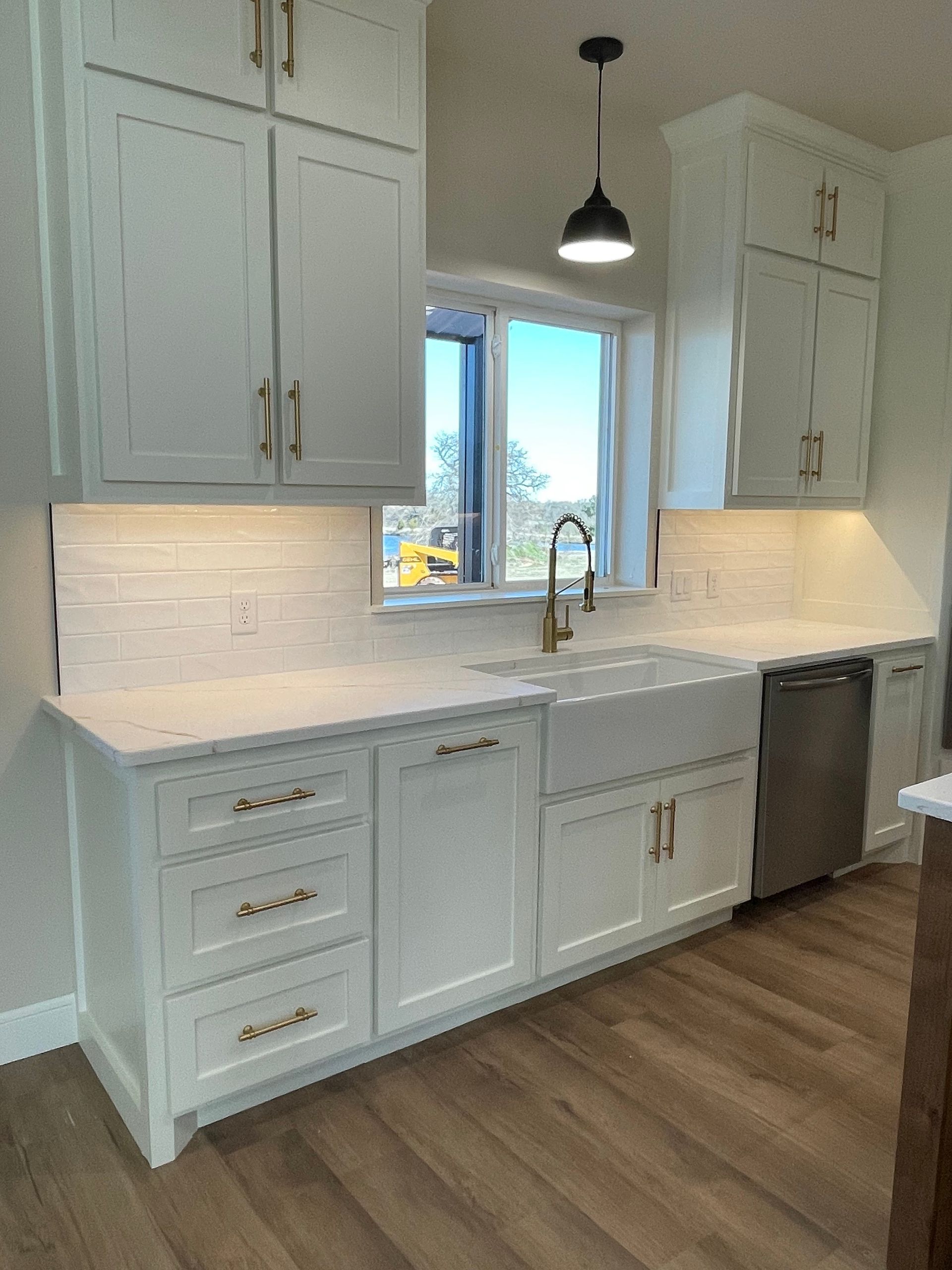 Bright white kitchen with cabinets, island sink, window, pendant light, and wood floor