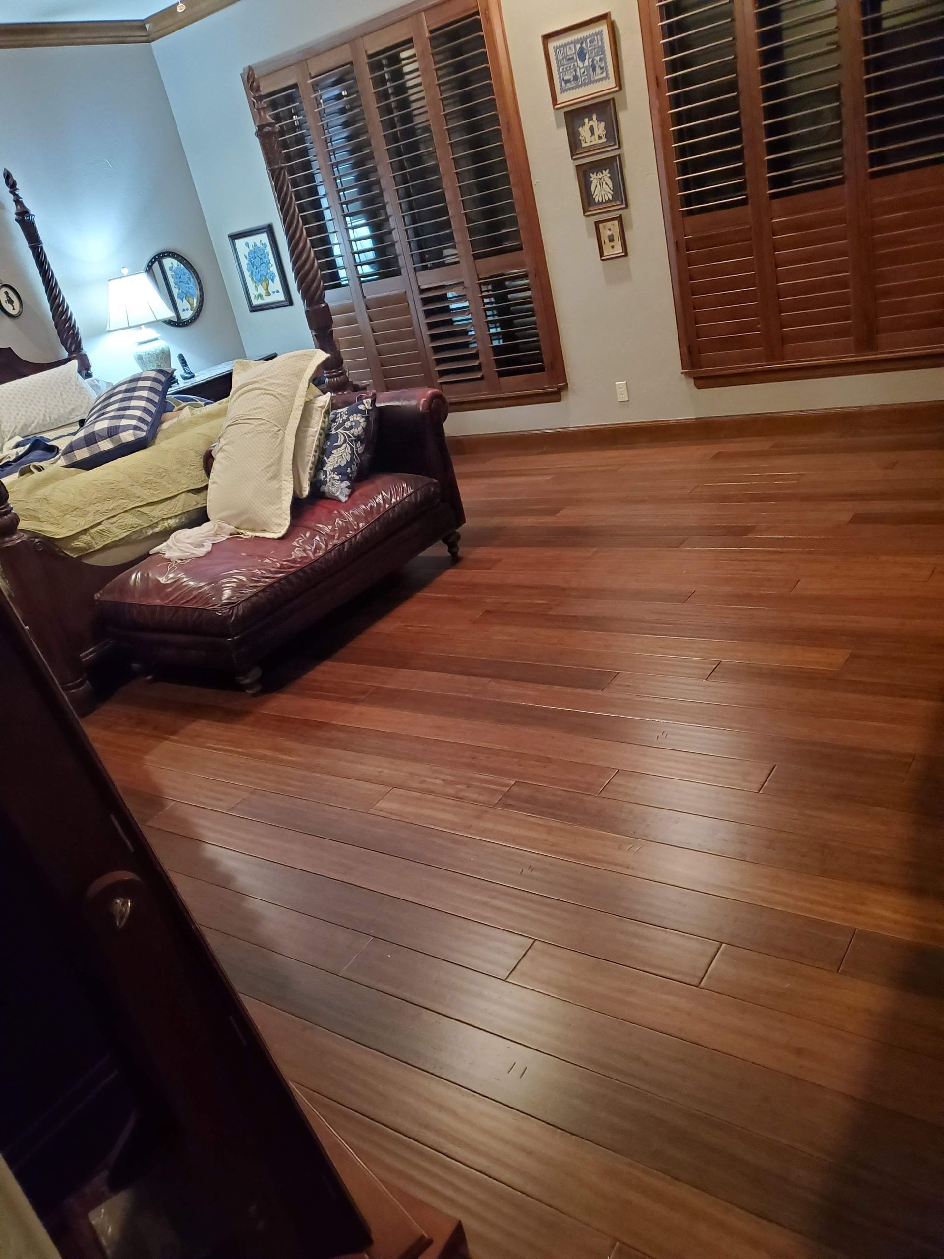 Empty living room with polished wooden floors, brown sofa, and tall shuttered windows.