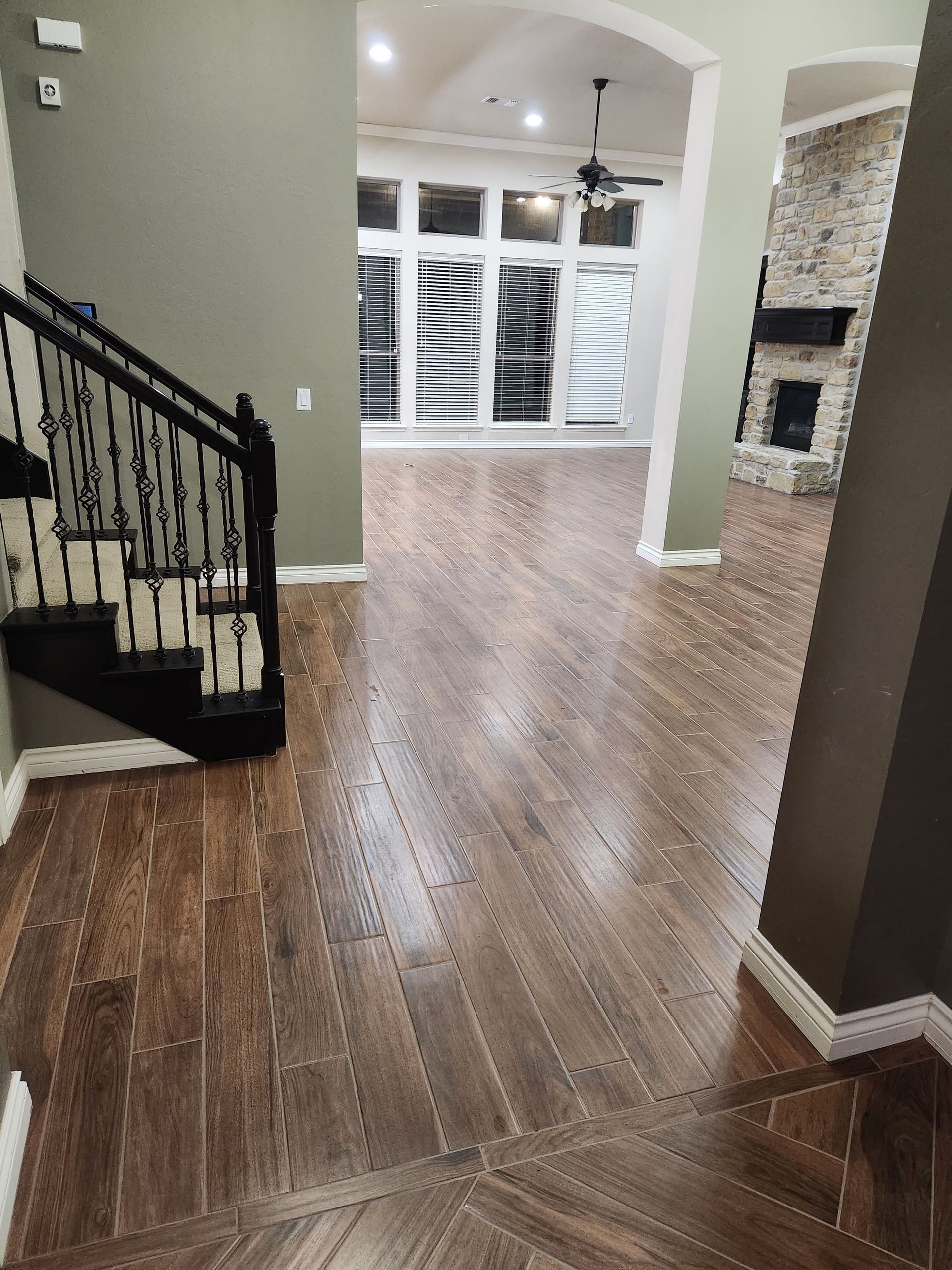 Empty living room with hardwood floors, staircase on left, and arched opening to a bright windowed area.