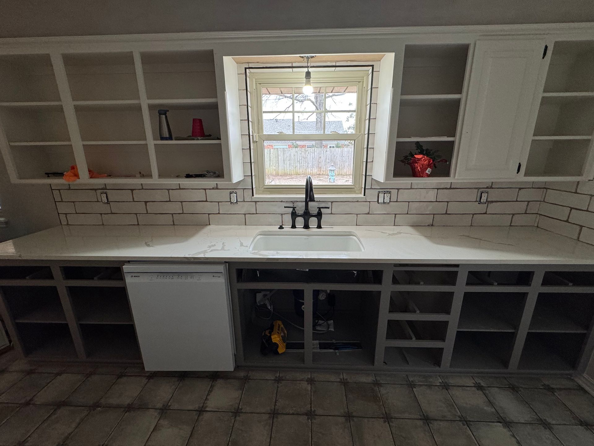 Built-in kitchen cabinets with white subway tile backsplash and a sink under a window
