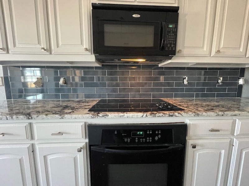 Kitchen with white cabinets, black microwave, electric stove, and gray tile backsplash