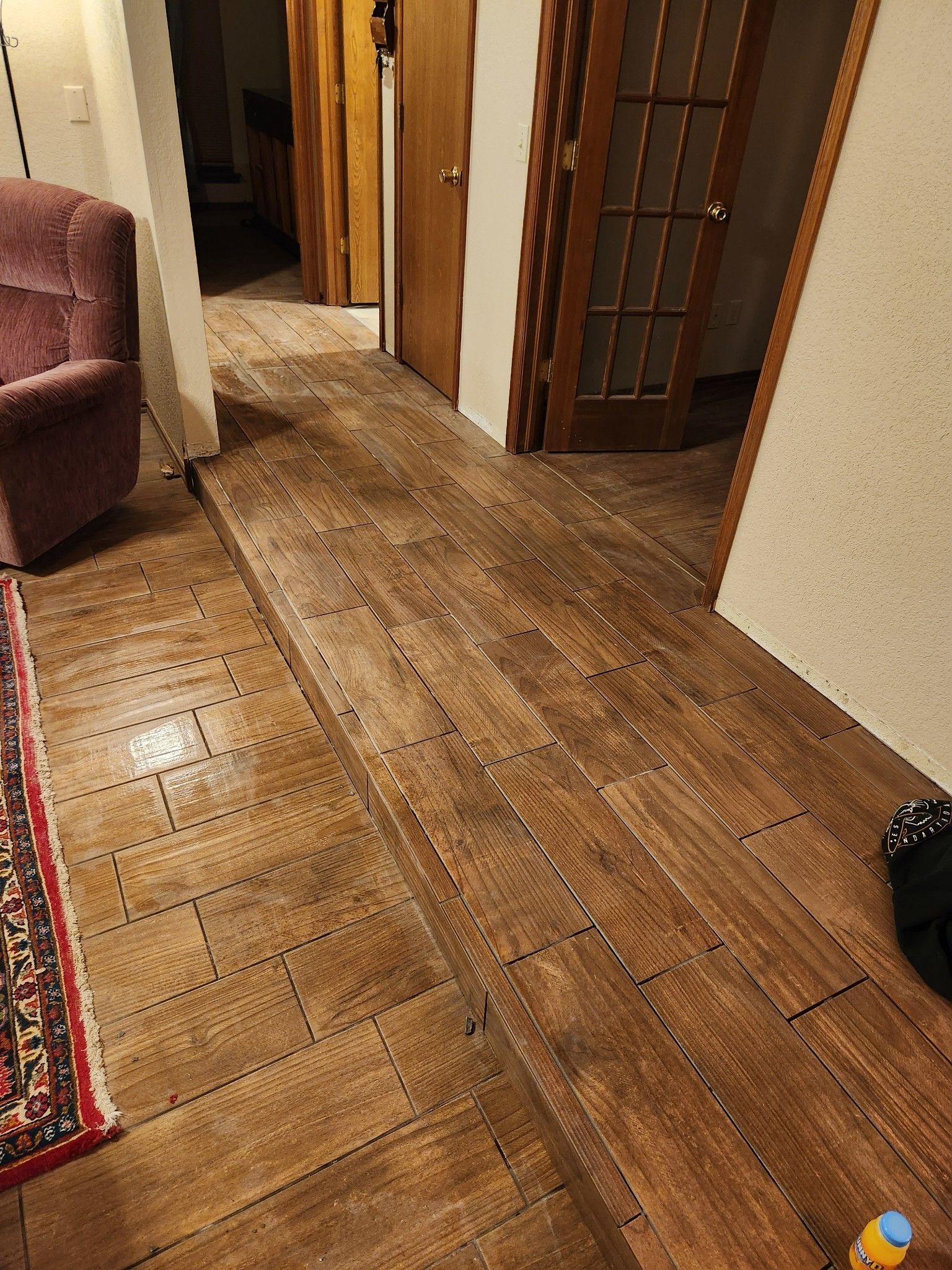 Long wooden hallway with doors, a rug edge, and a couch in the corner