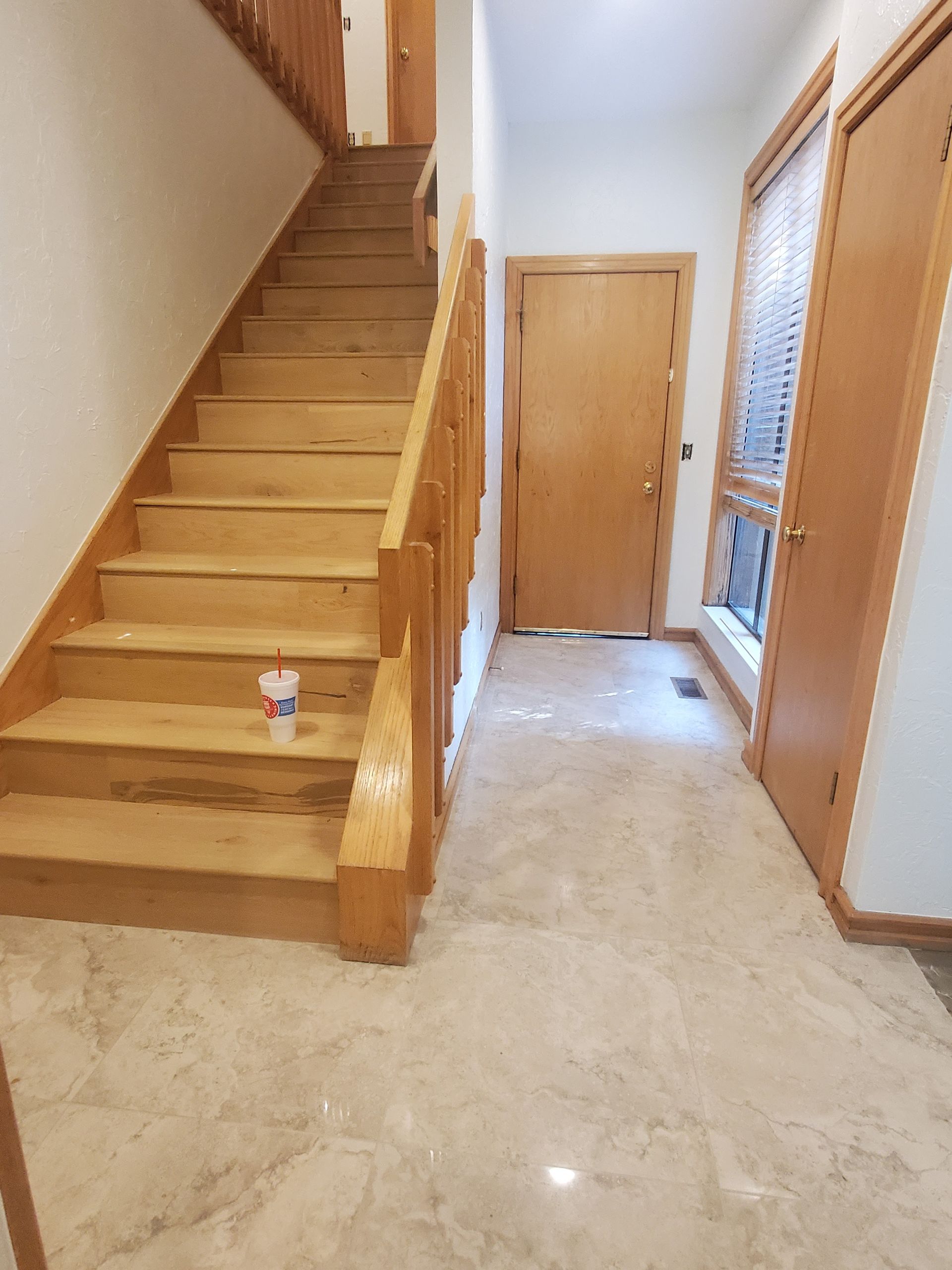 Hallway with wooden staircase, closed door at end, and a small figurine on the floor.