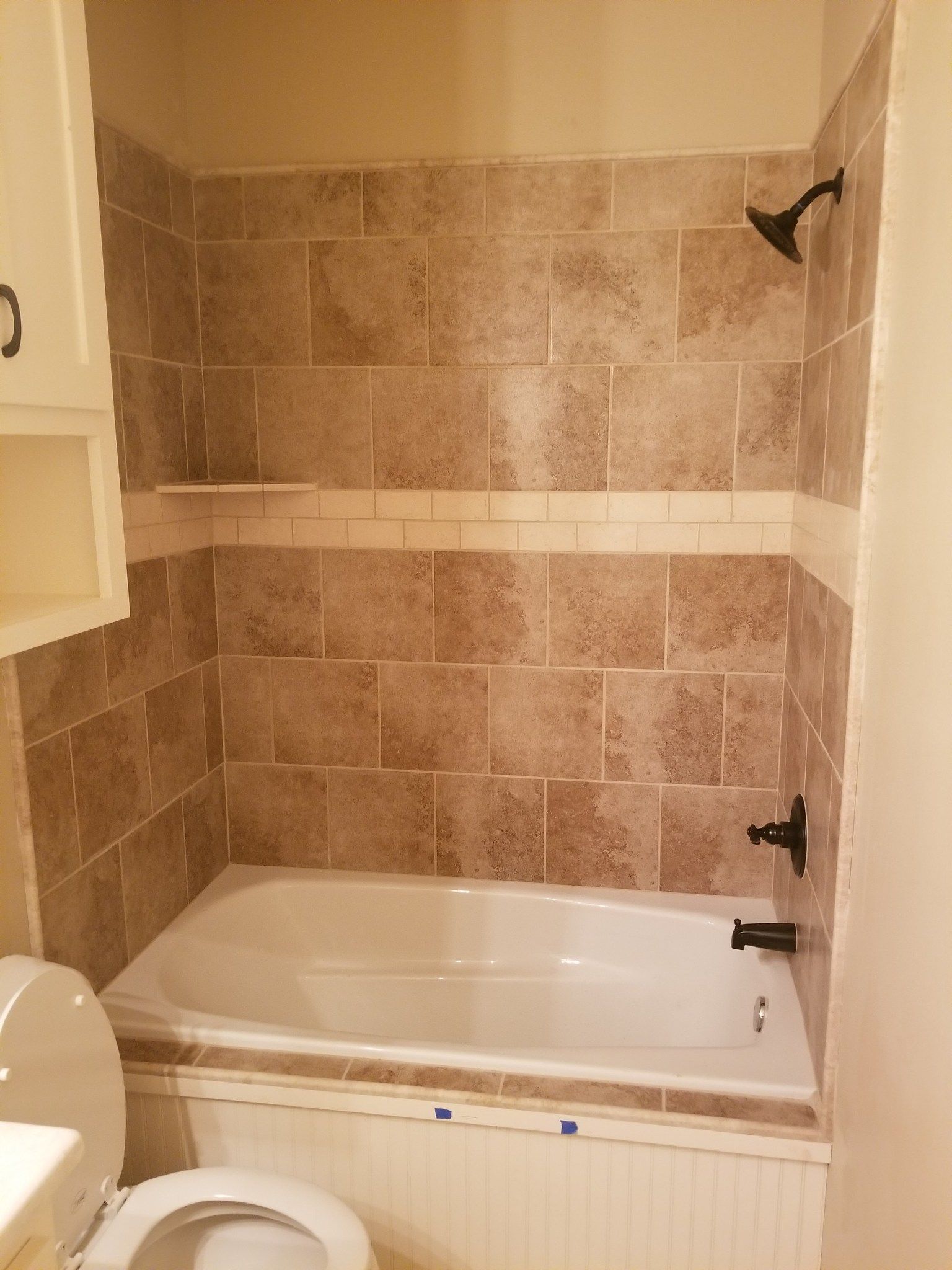 Tiled bathroom with white bathtub, tan walls, and shower fixtures on the right.