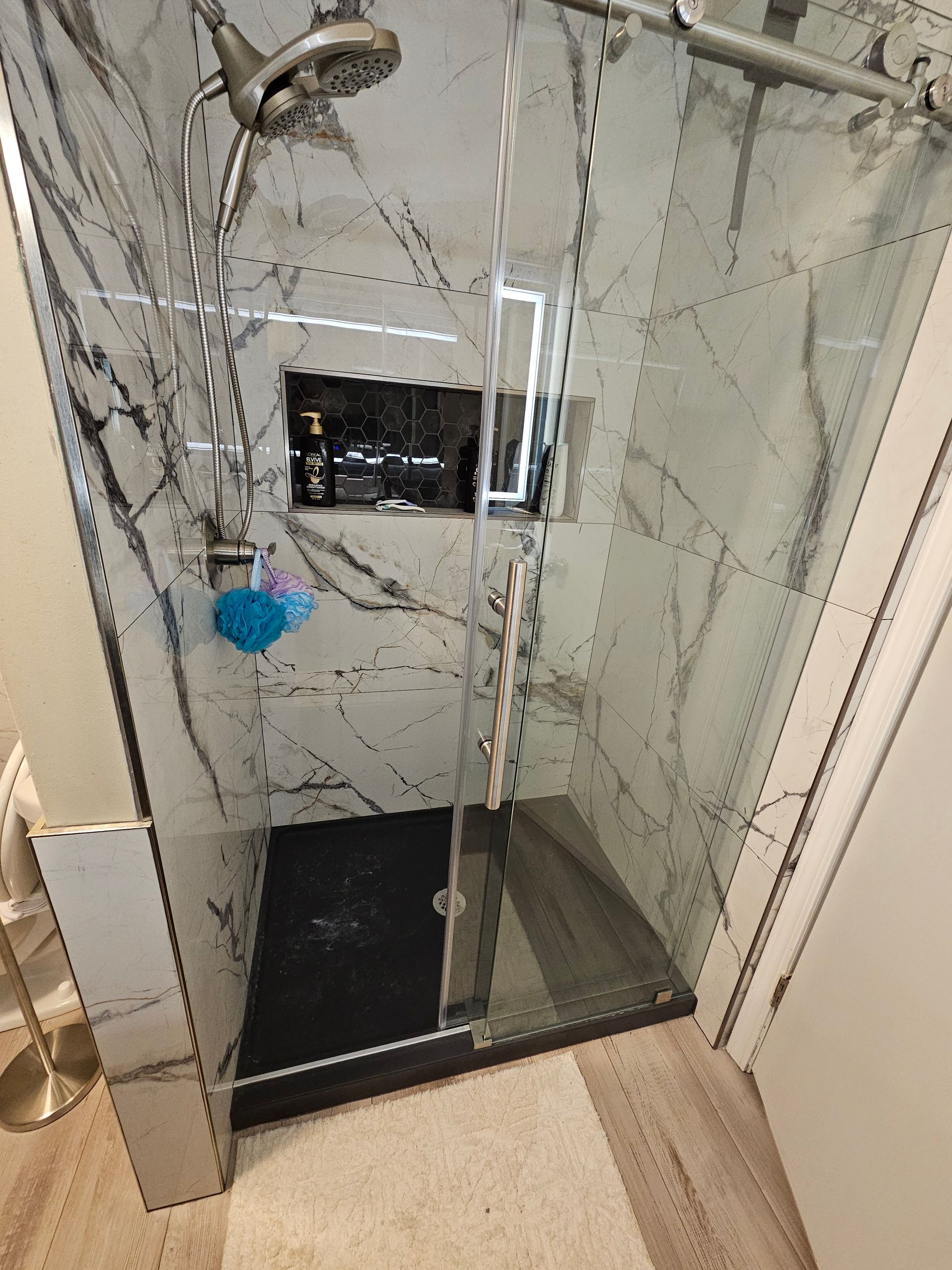 Marble-tiled shower stall with a blue shower cap hanging on the left wall.