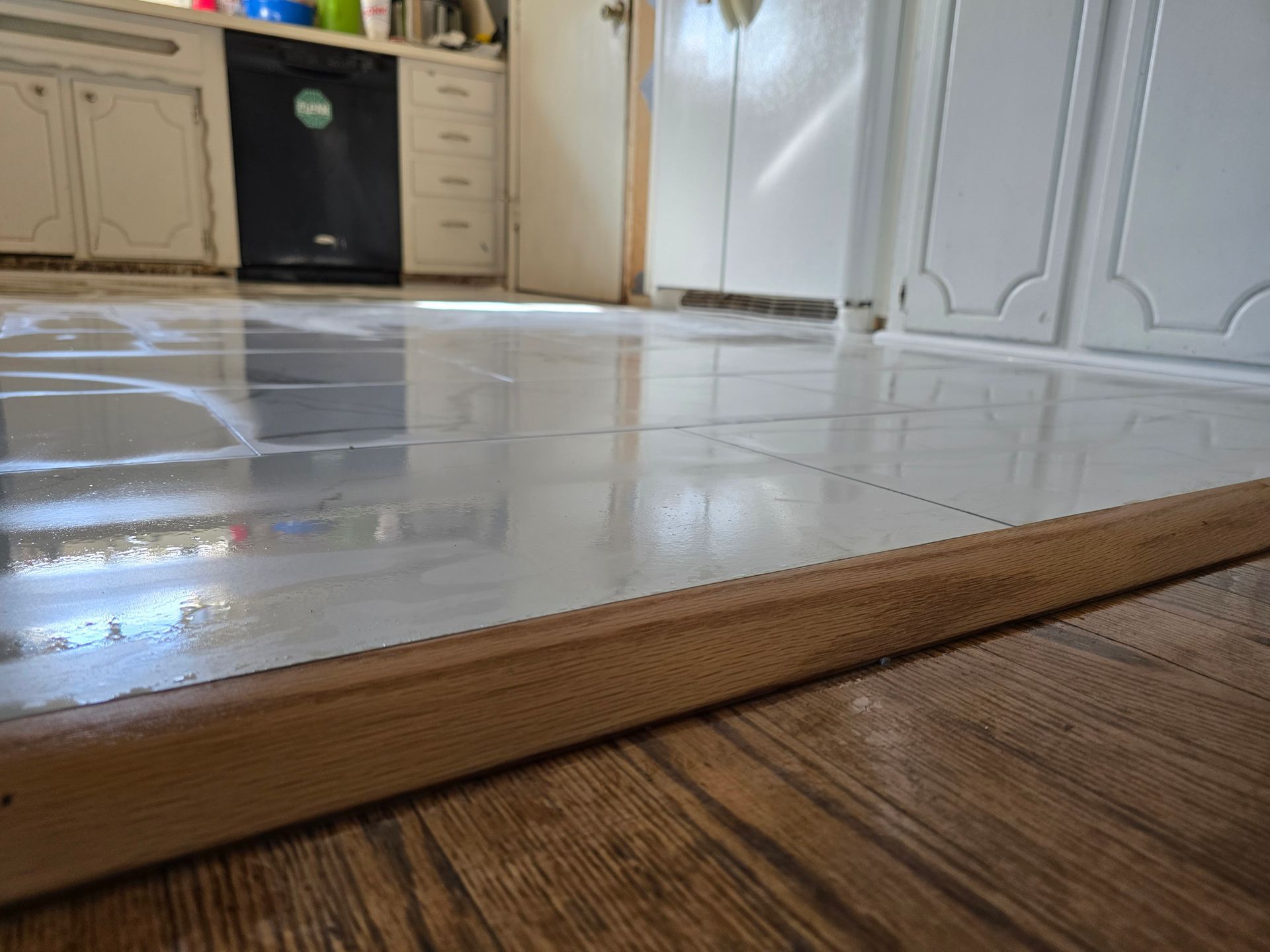 Kitchen floor with a glossy tiled step edge and wood flooring in the foreground
