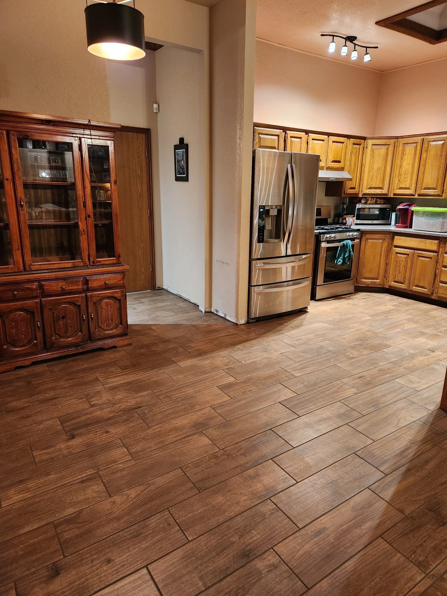 Empty kitchen and dining area with wooden floor, wood cabinets, stainless fridge, and hanging light fixture