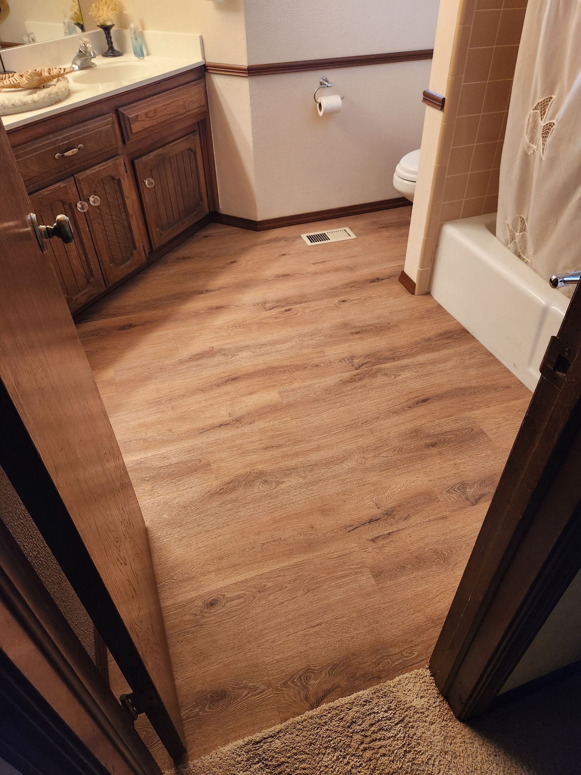 Bathroom with wood-look flooring, vanity sink, and bathtub shower curtain in a beige interior