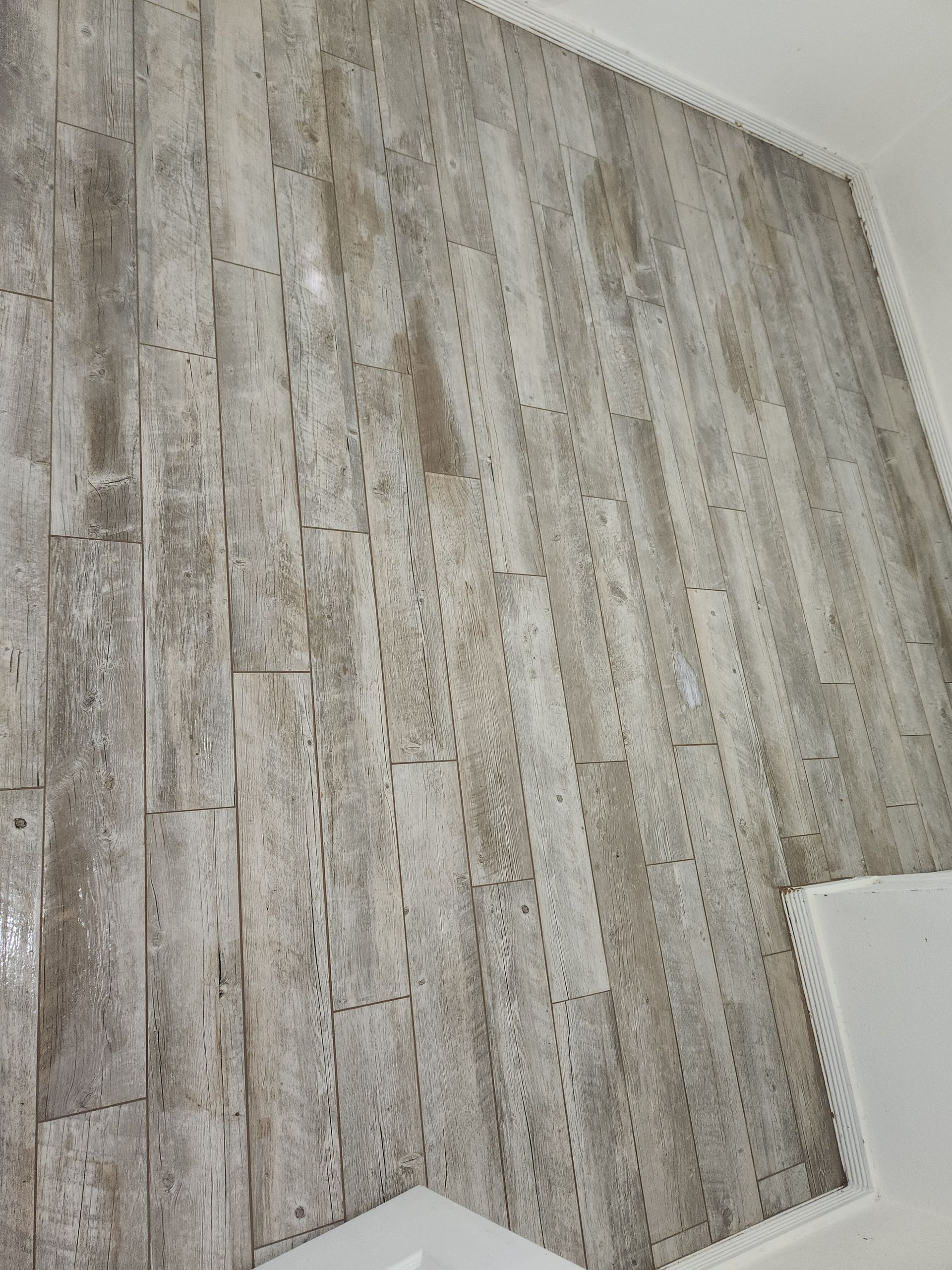 Gray wood-look flooring with a white baseboard corner and a small white vent at the lower right.