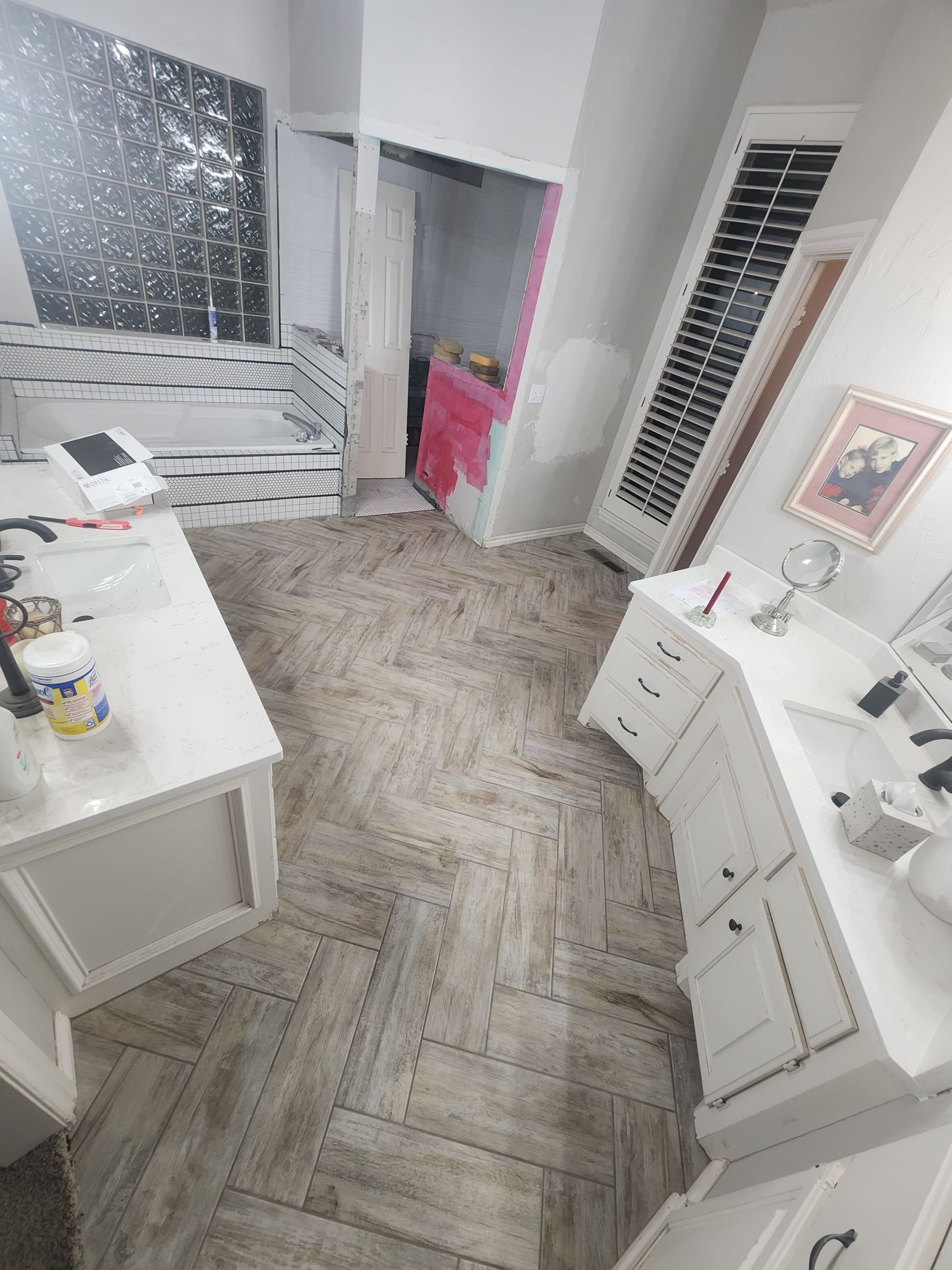 Bright vanity room with white furniture, herringbone floor, and a pink chair by an open closet.