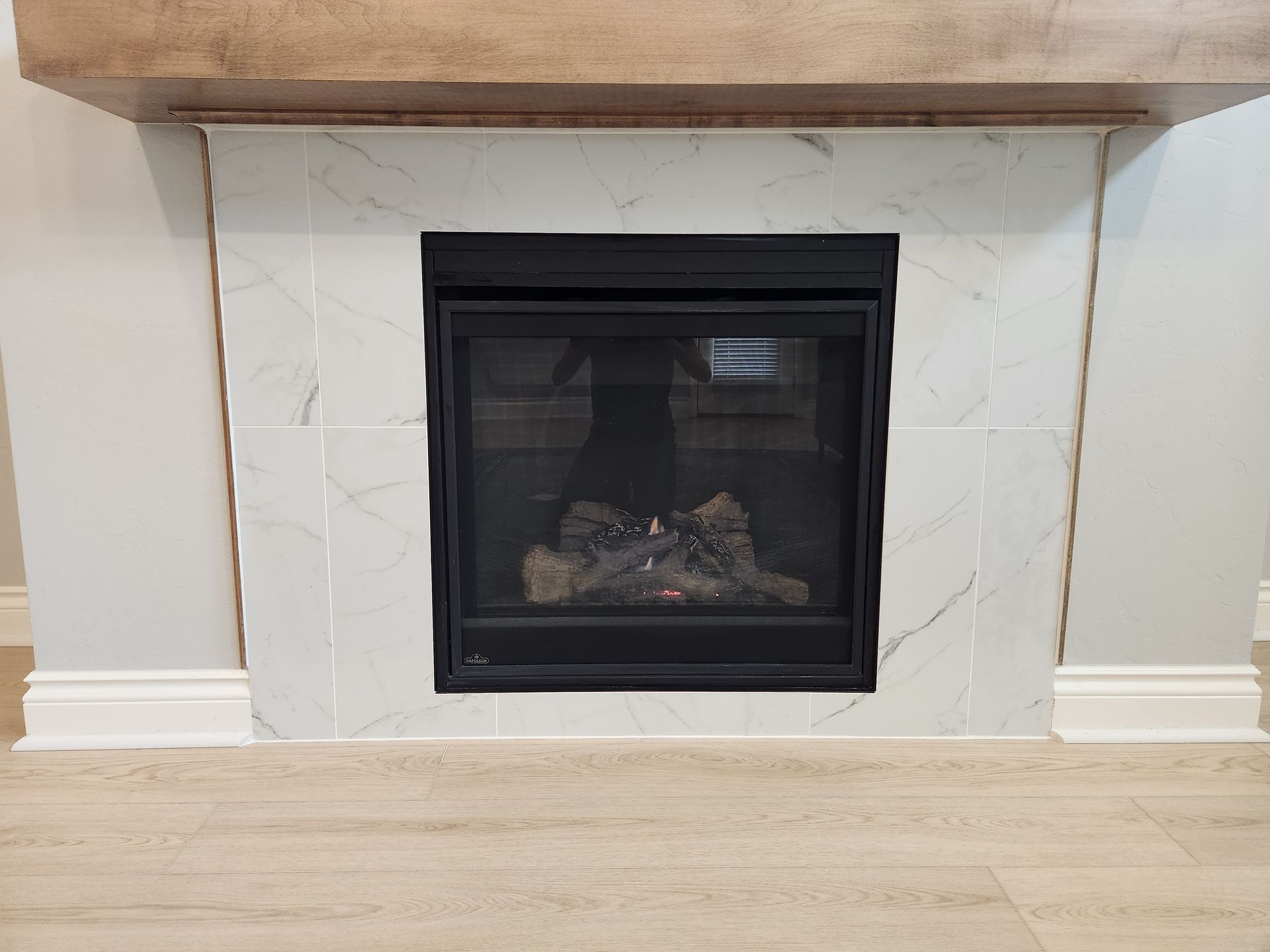 Modern fireplace with black glass insert, white stone surround, and wood mantel in a light room