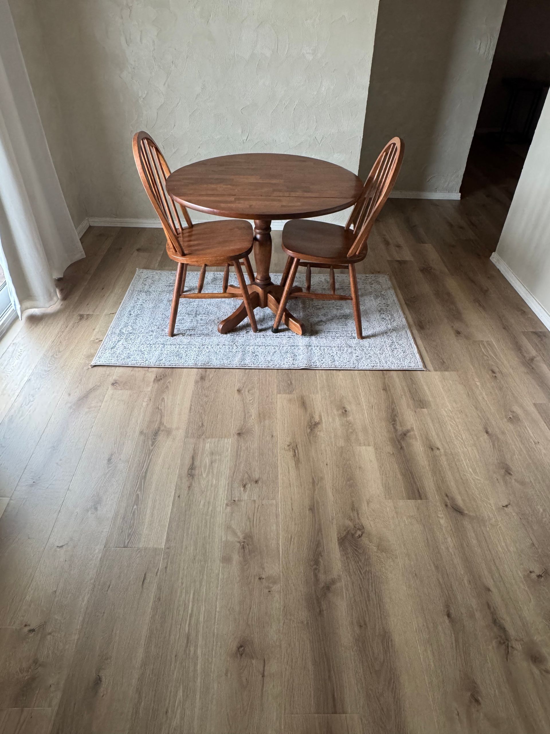 Small round wooden table with two woven chairs on a light rug in a modern dining nook.