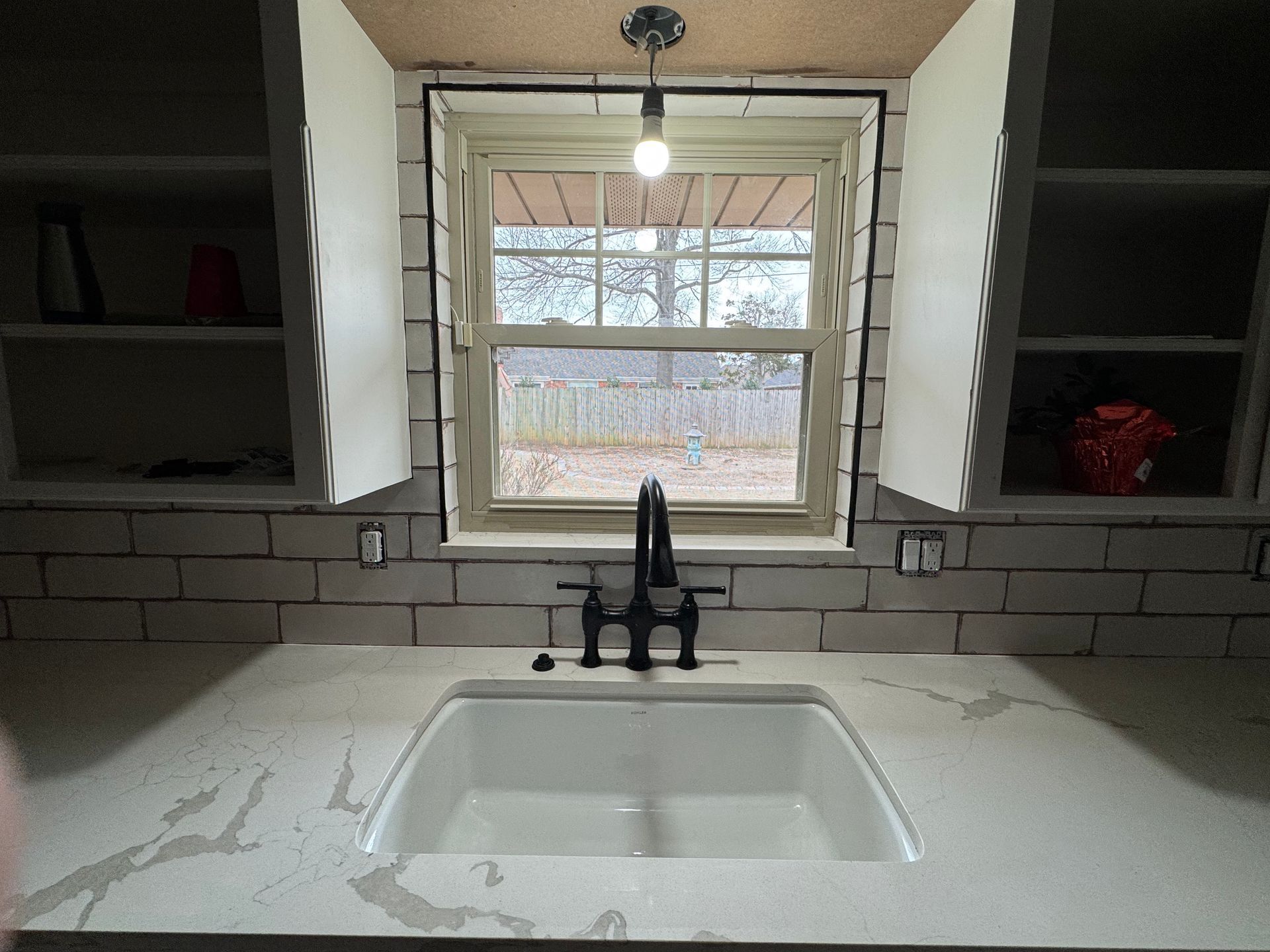 Kitchen sink beneath a window, with white countertop and dark cabinets on either side.