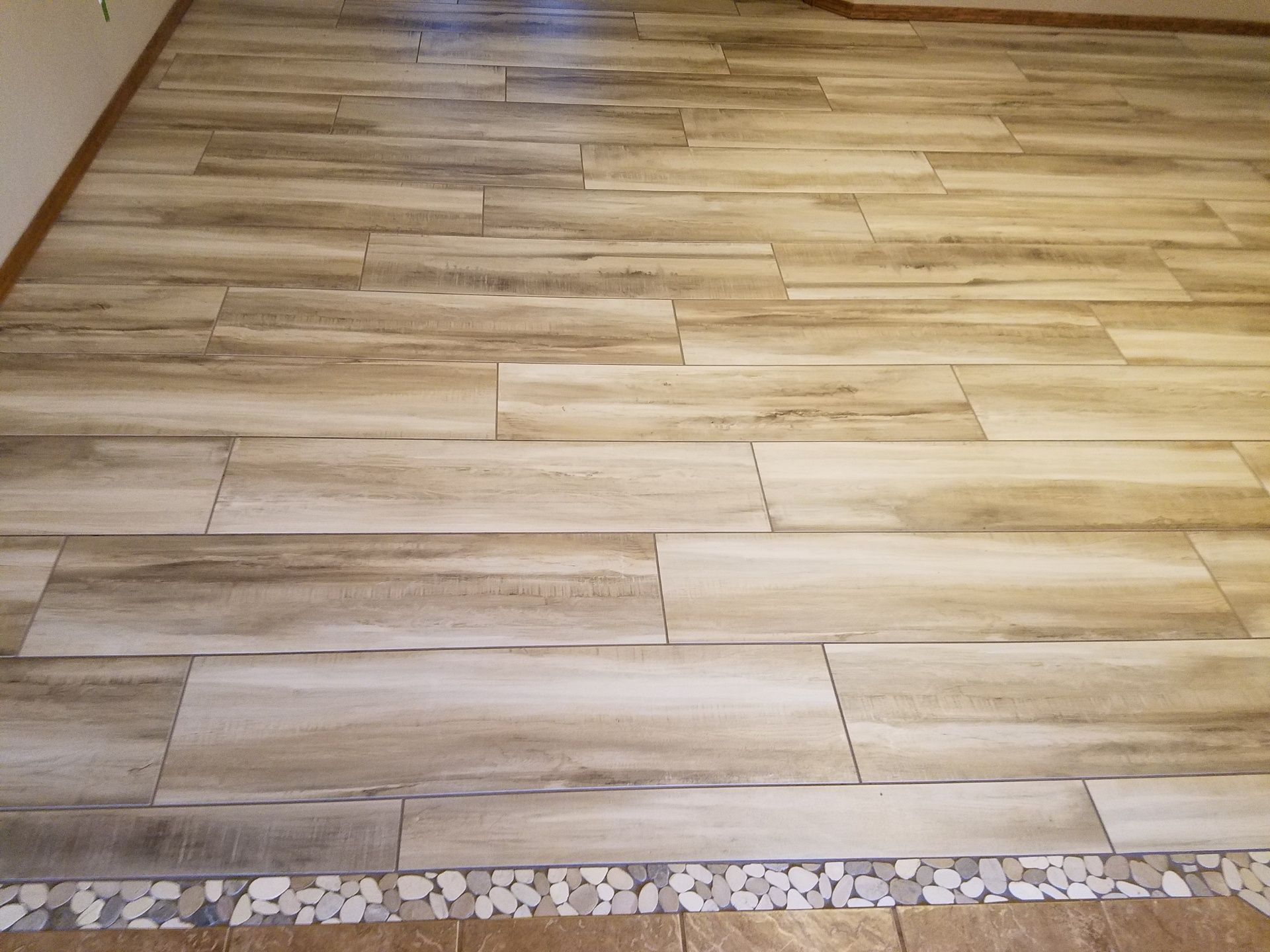 Light wood plank flooring with a narrow mosaic tile border along the bottom edge.