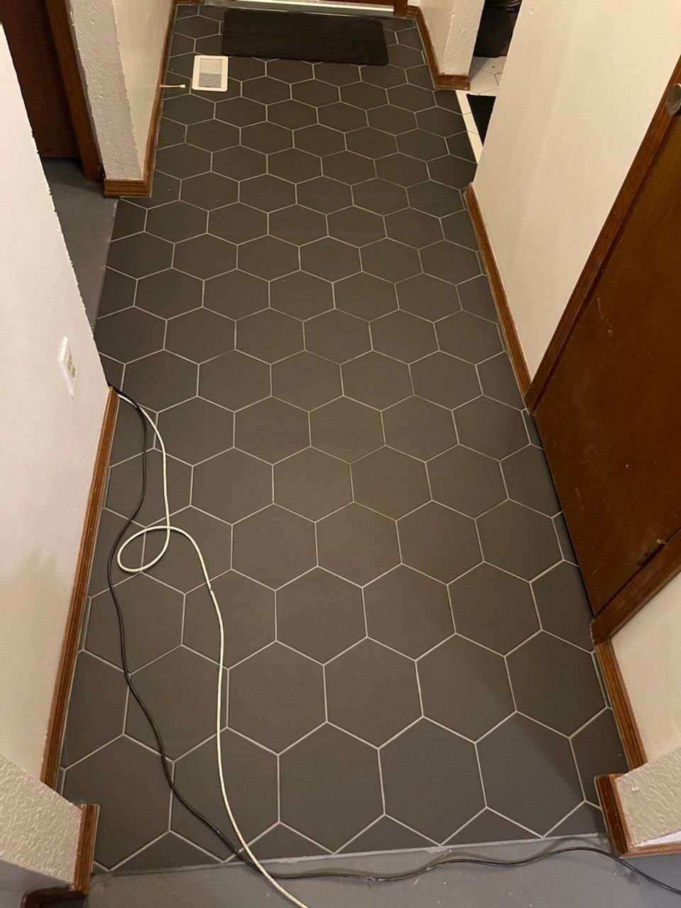 Narrow hallway with dark hex-pattern carpet and loose cables along the left side.