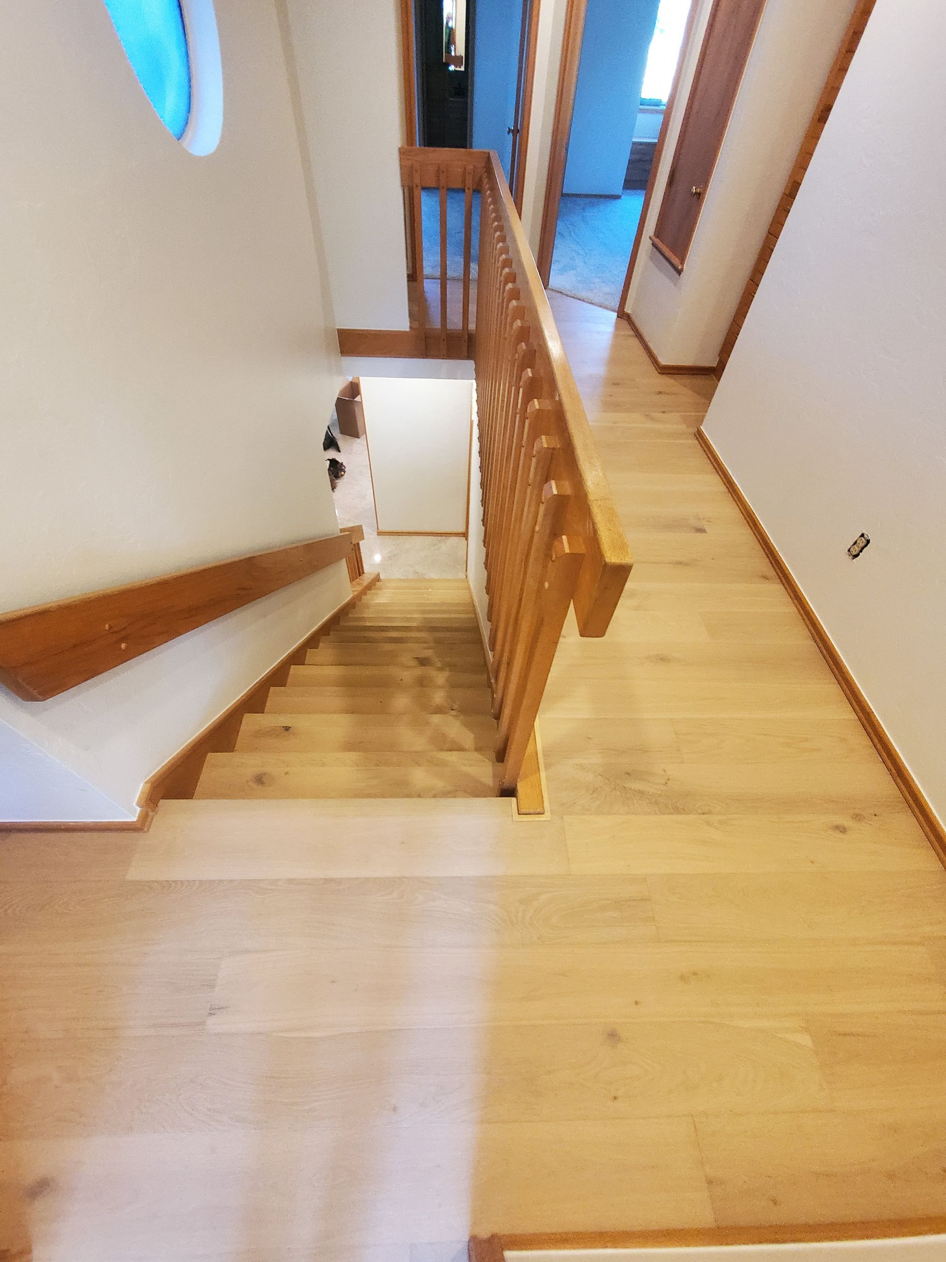 Stairwell with light wood steps and railing in a modern home, viewed from the landing.