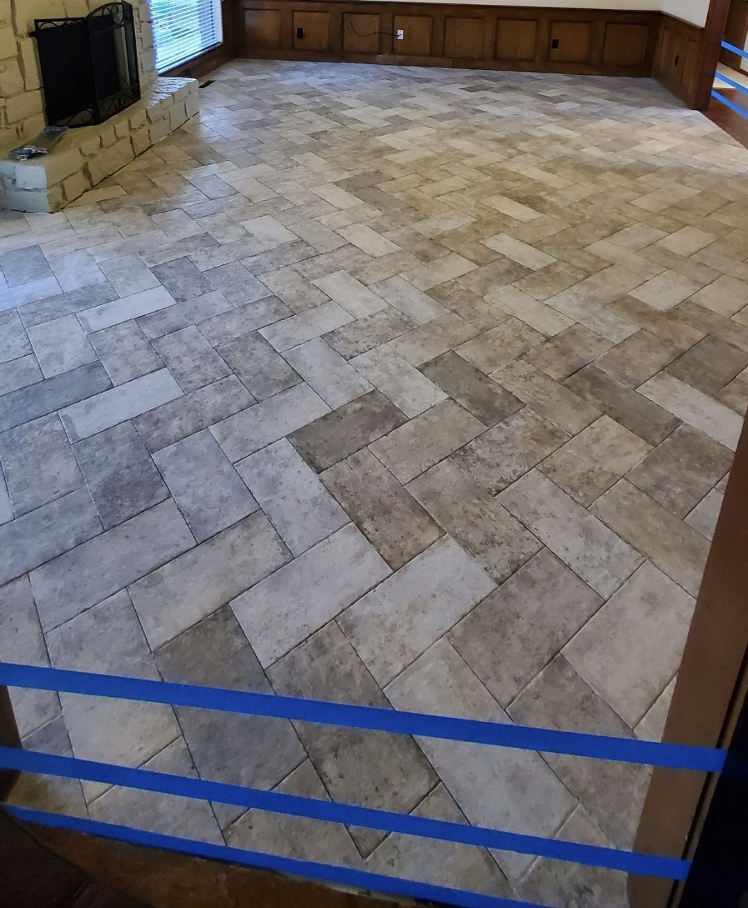 Empty room with stone-tile floor, wood cabinets, a fireplace, and blue tape across the foreground