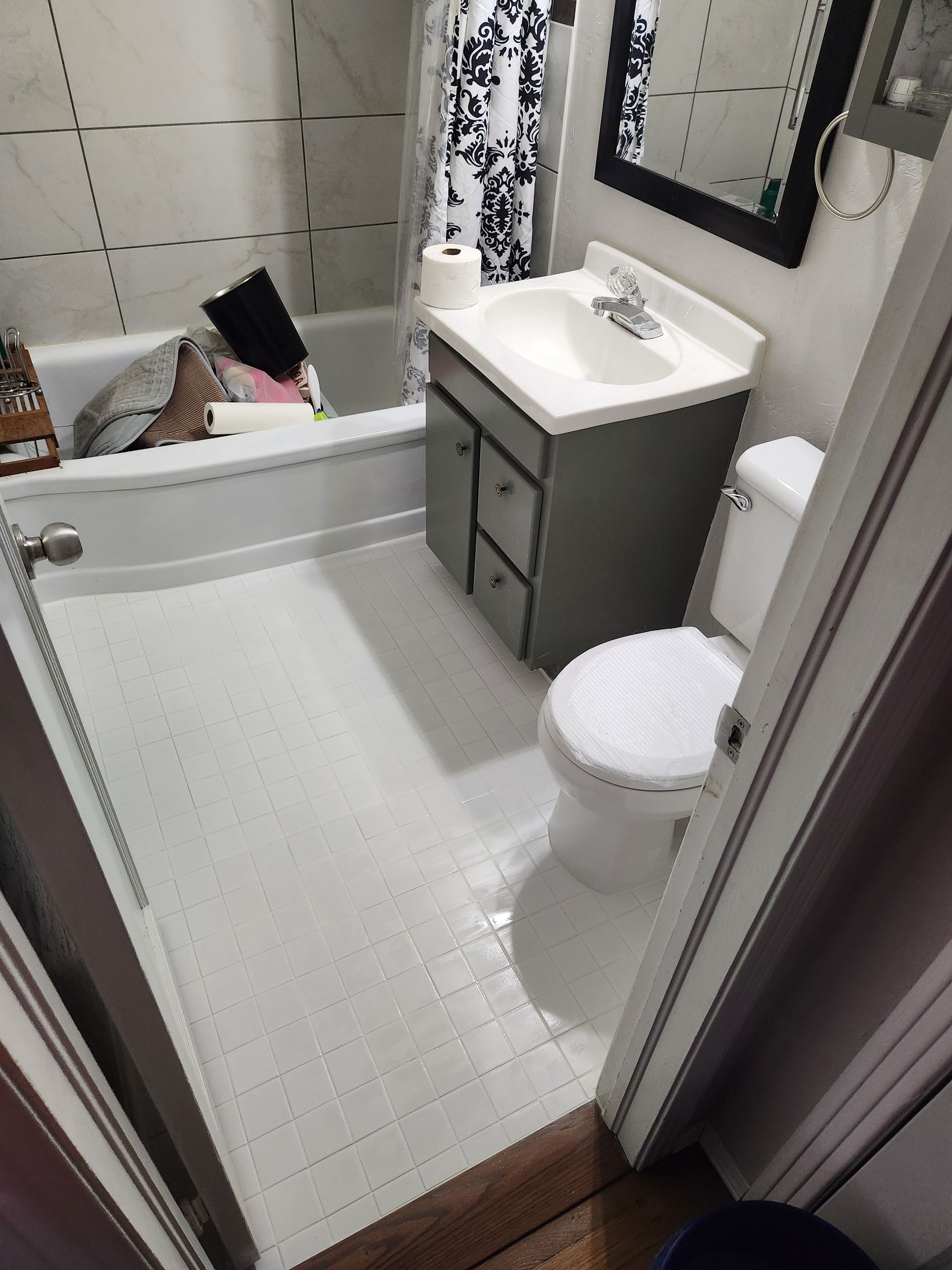 Small bathroom with white tub, toilet, sink cabinet, shower curtain, and tiled floor.