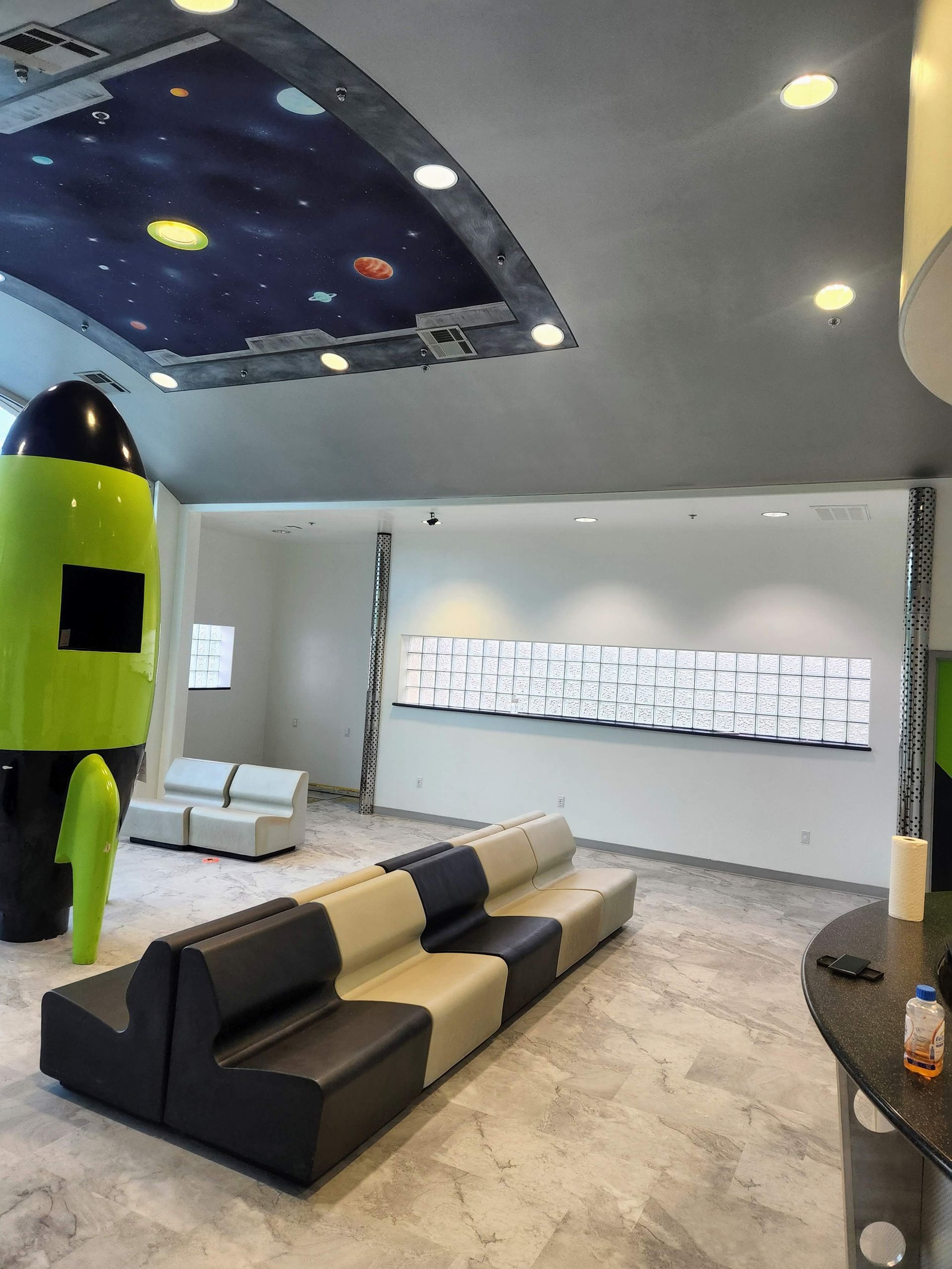 Modern lounge with a rocket-shaped decor, curved black-and-beige seating, and a starry ceiling mural.