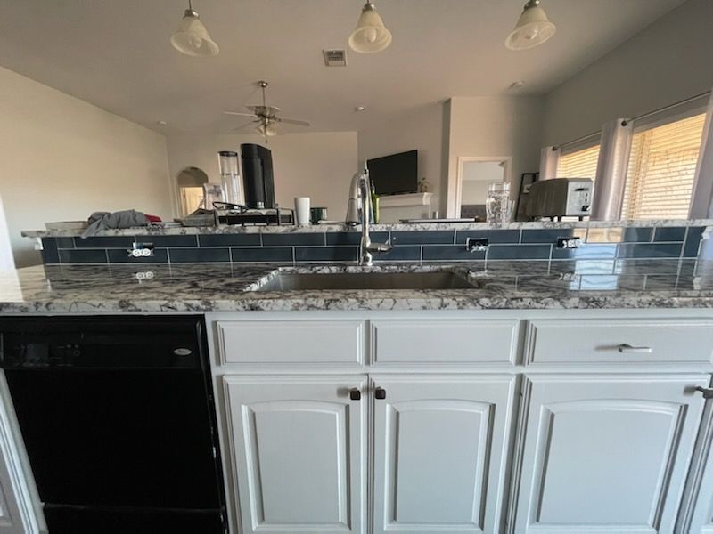 Kitchen view with white cabinets, granite countertop, and pendant lights open to a living area