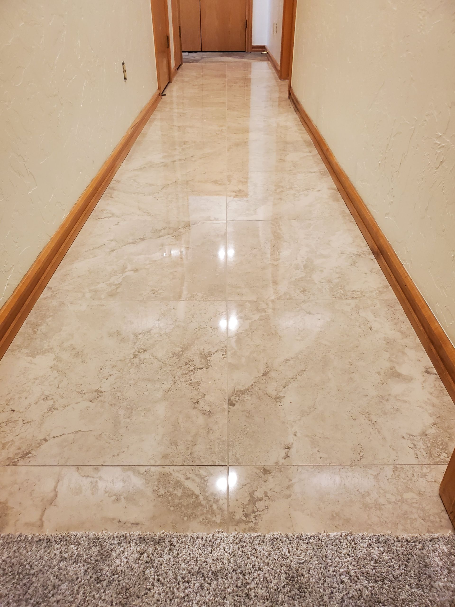 Long polished hallway with beige walls, wood trim, and a reflective marble floor leading to a closed door