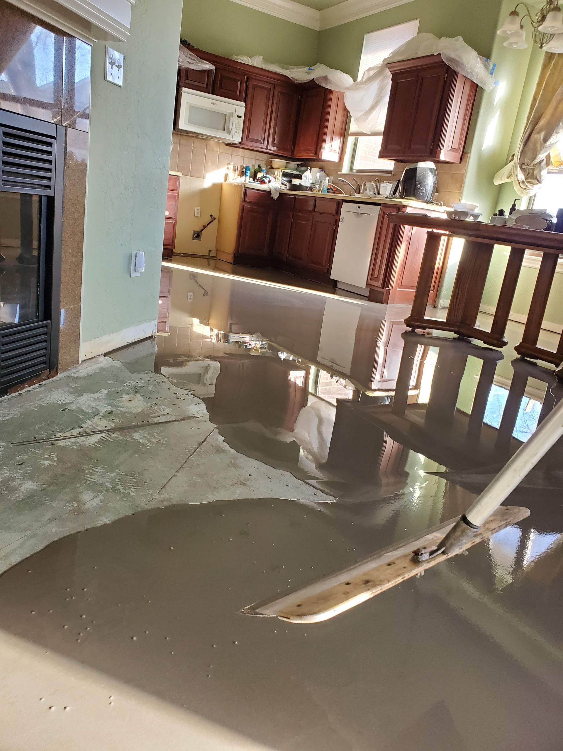 Flooded kitchen with standing water reflecting cabinets and a broken floor section in the foreground