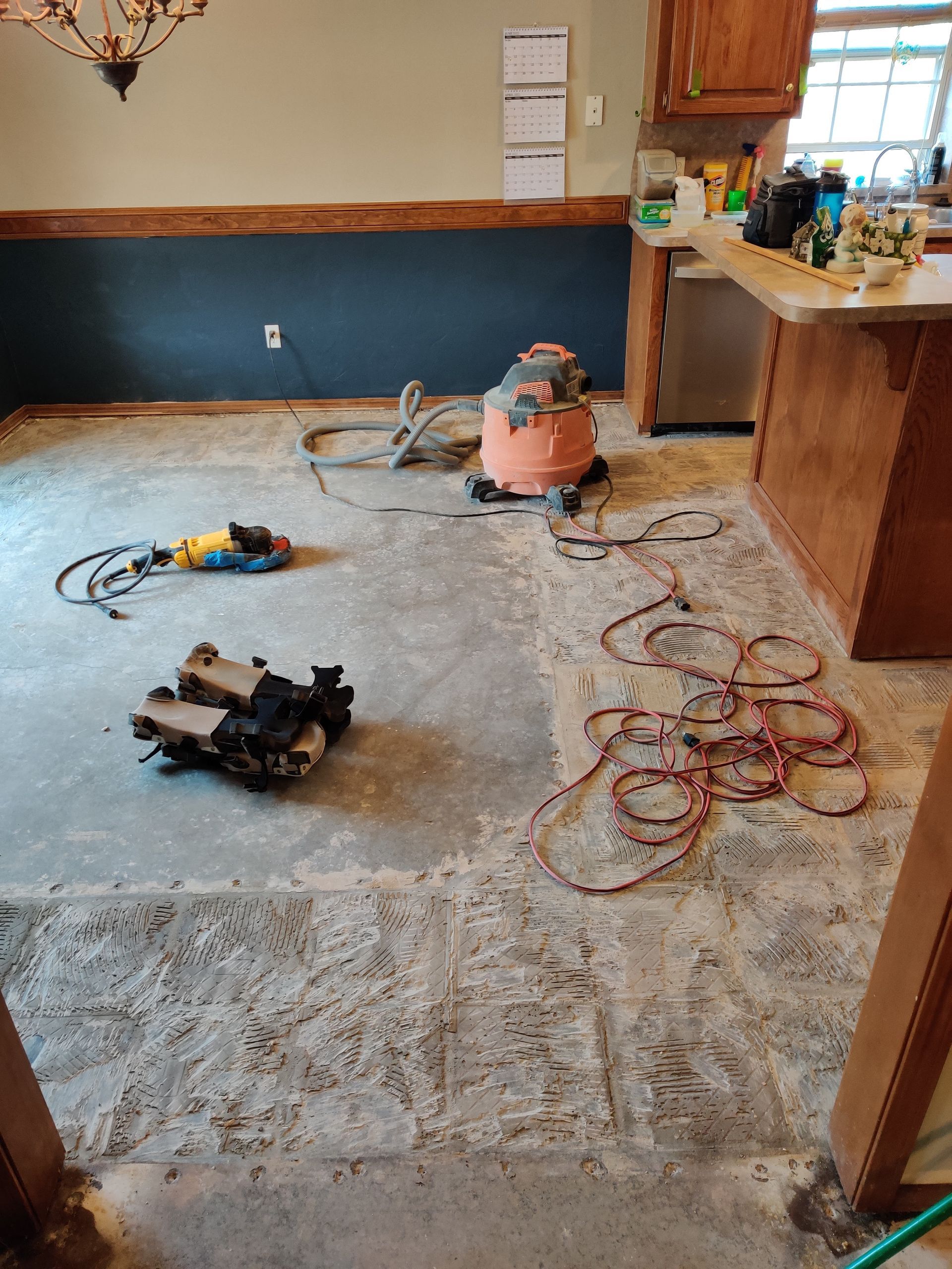 Messy kitchen under renovation with power tools, cords, and dust on the floor
