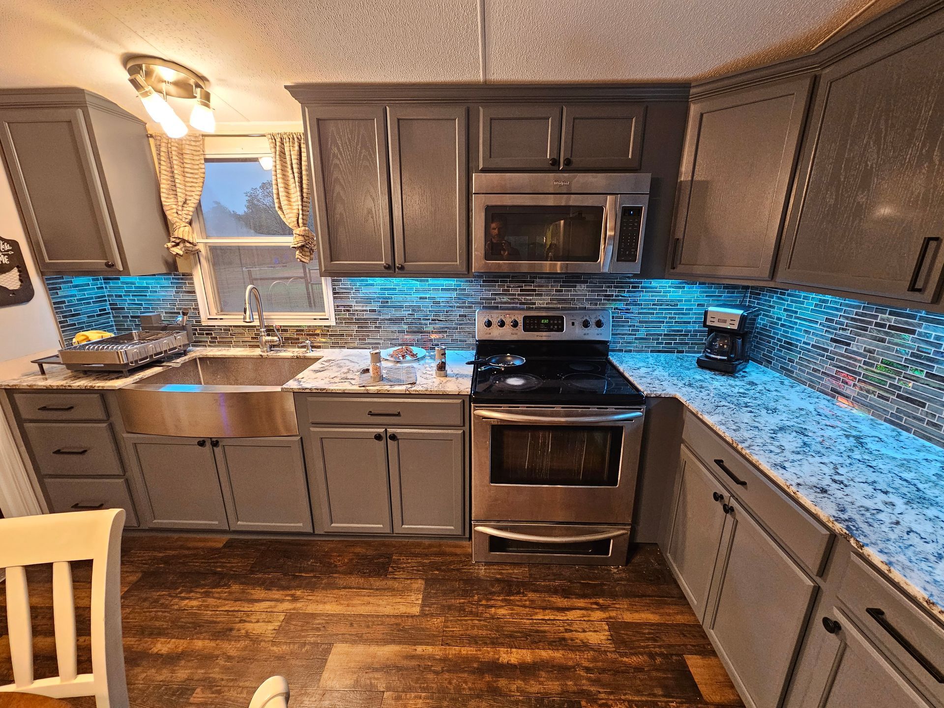 Modern kitchen with dark cabinets, stainless appliances, blue backsplash, and wooden floor
