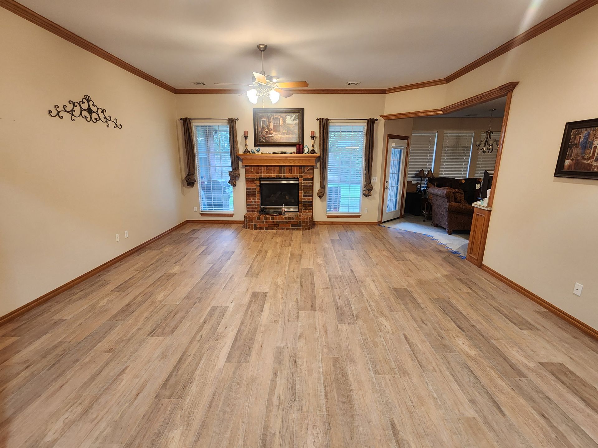 Empty living room with light wood floors, beige walls, and a fireplace between two windows.