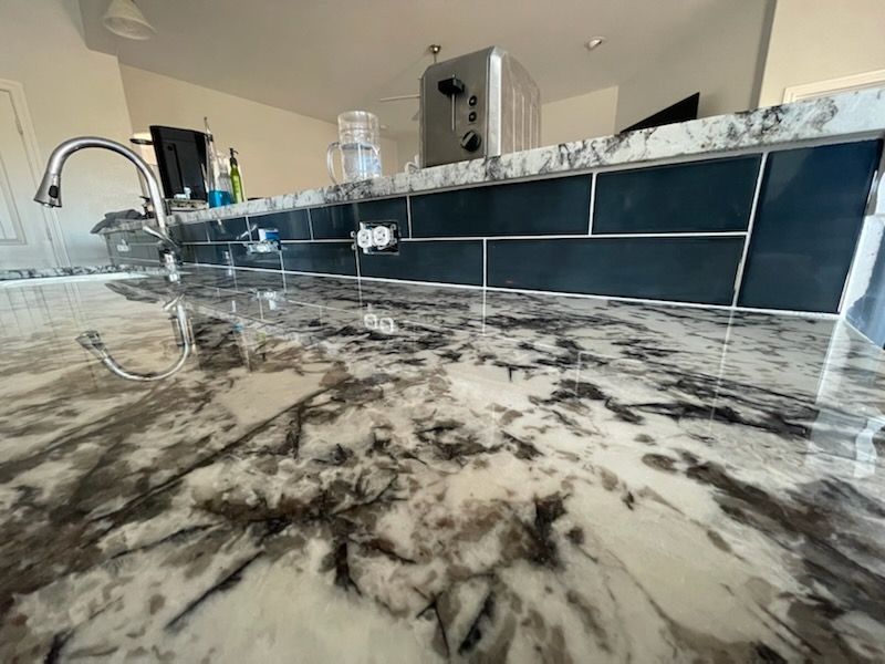 Kitchen with glossy marble countertop and black tiled backsplash, shown at a low angle.