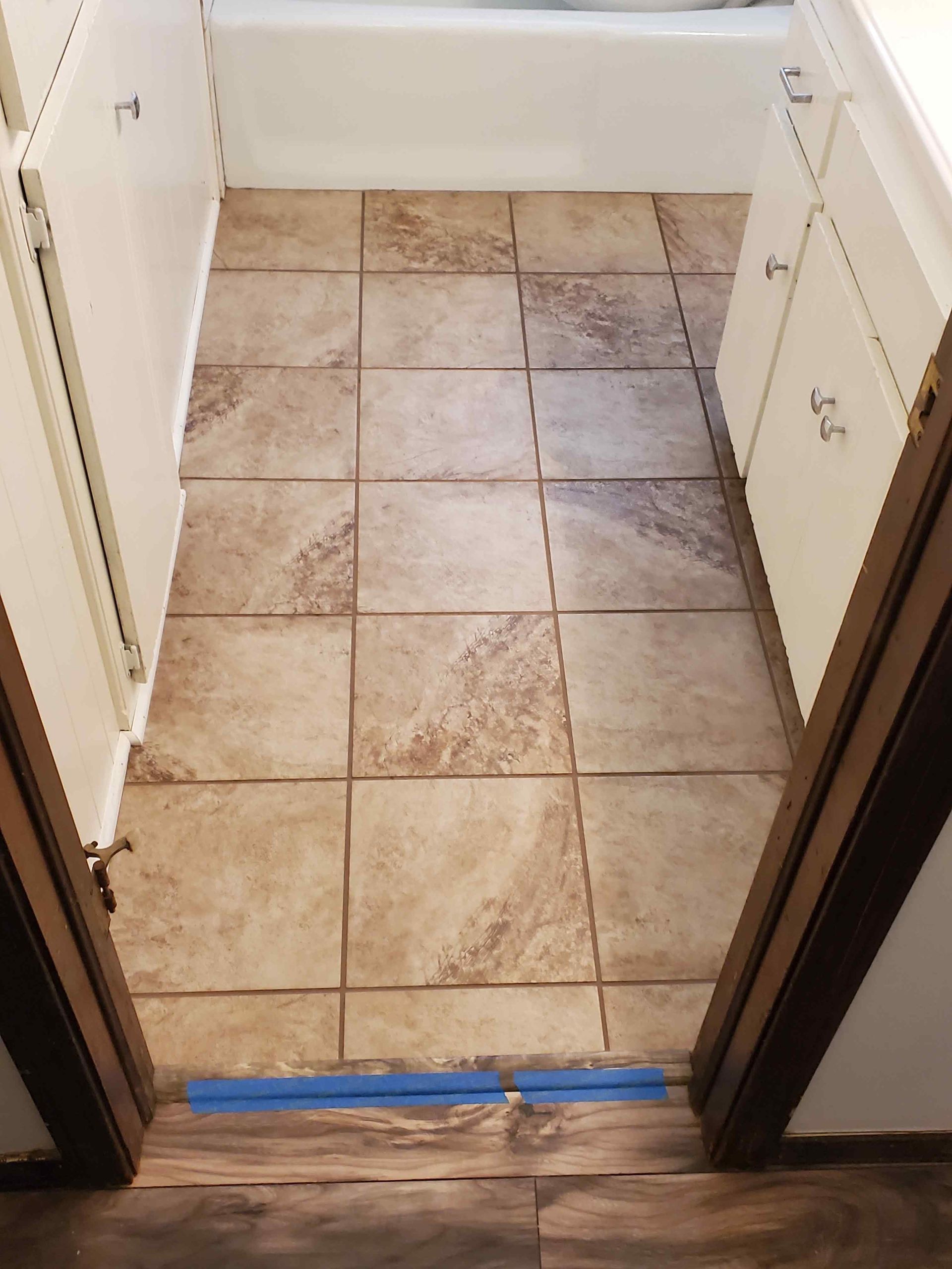 Narrow tiled bathroom floor area with a blue tape strip across the doorway