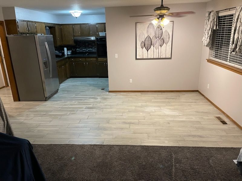 Empty living/dining room with light wood floor, gray walls, kitchen in back, and ceiling fans.