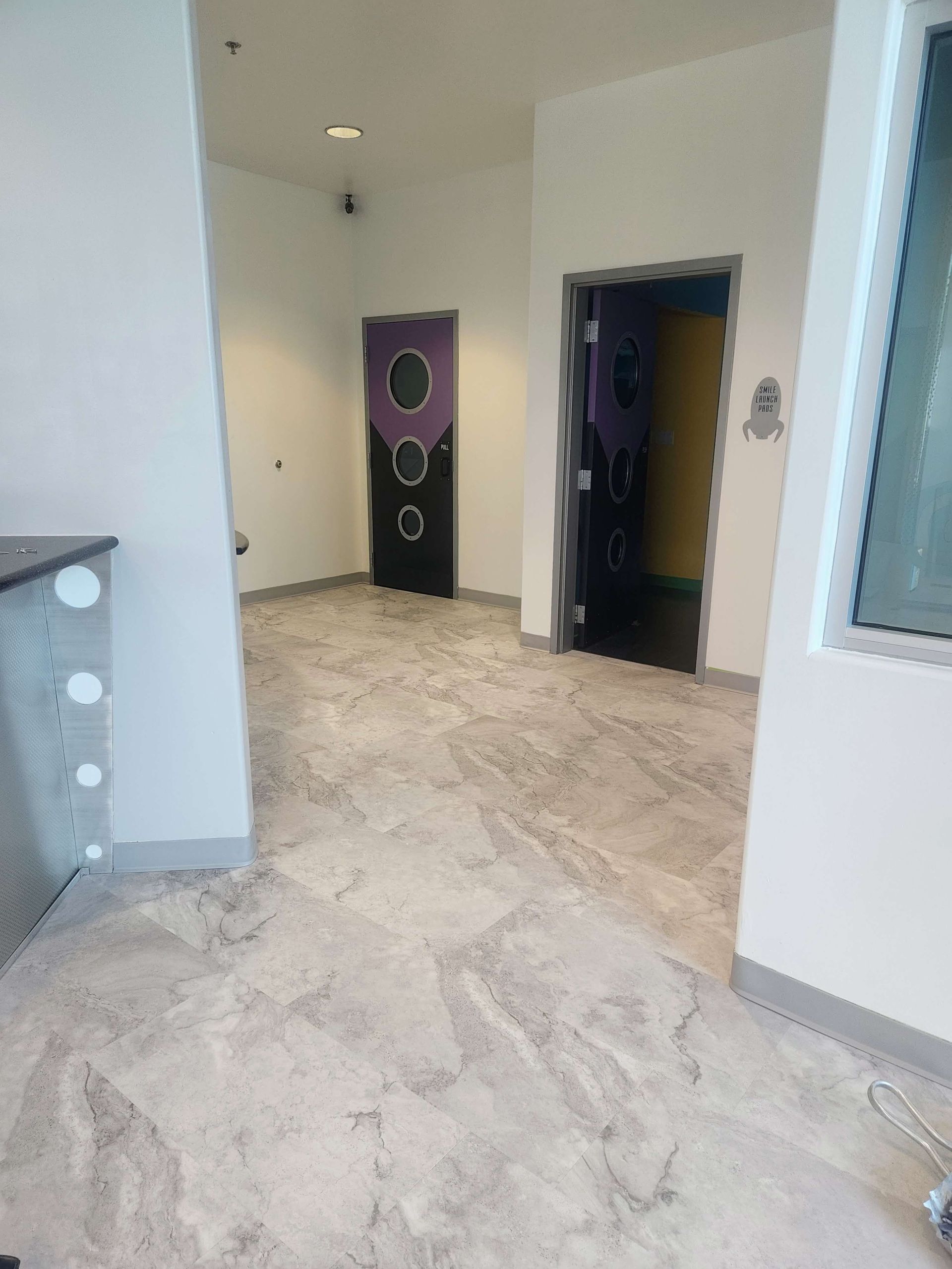 Empty modern hallway with light stone floor, white walls, and dark doorways.