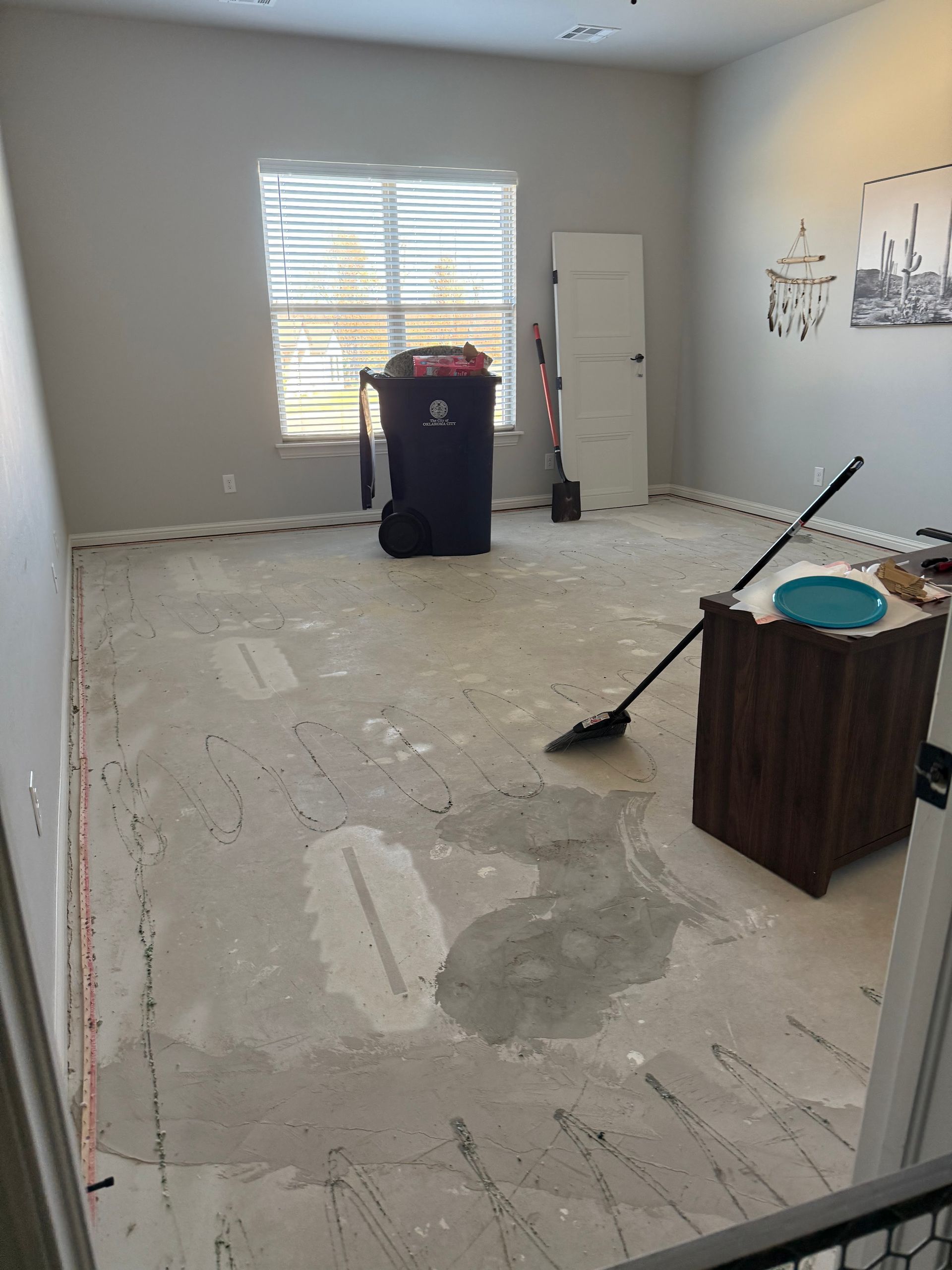 Empty room with bare concrete floor, window, trash bin, and cleaning tools during renovation