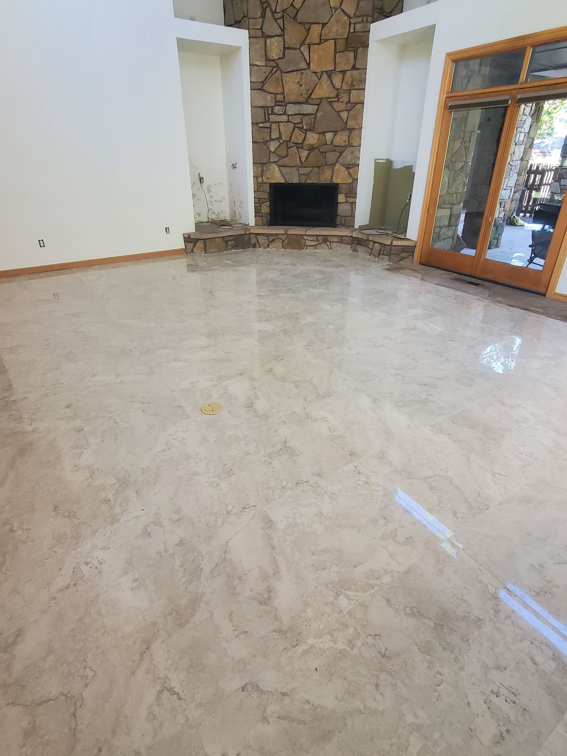 Empty living room with glossy marble floor, stone fireplace, and large glass doors.