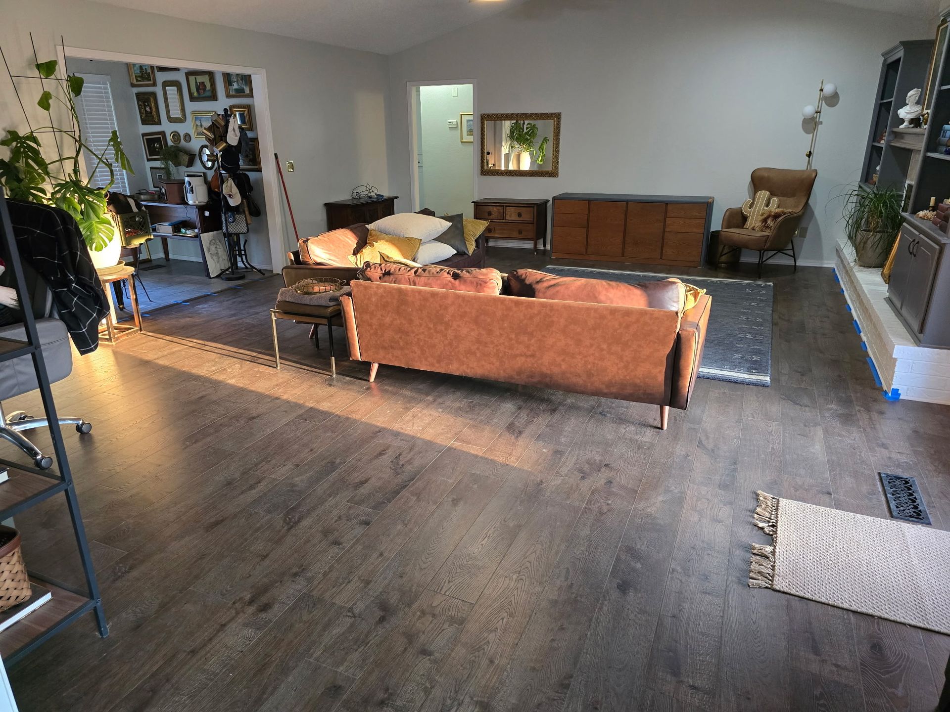 Modern living room with brown sofa, dark wood floors, rug, wall art, and dining area in the back.