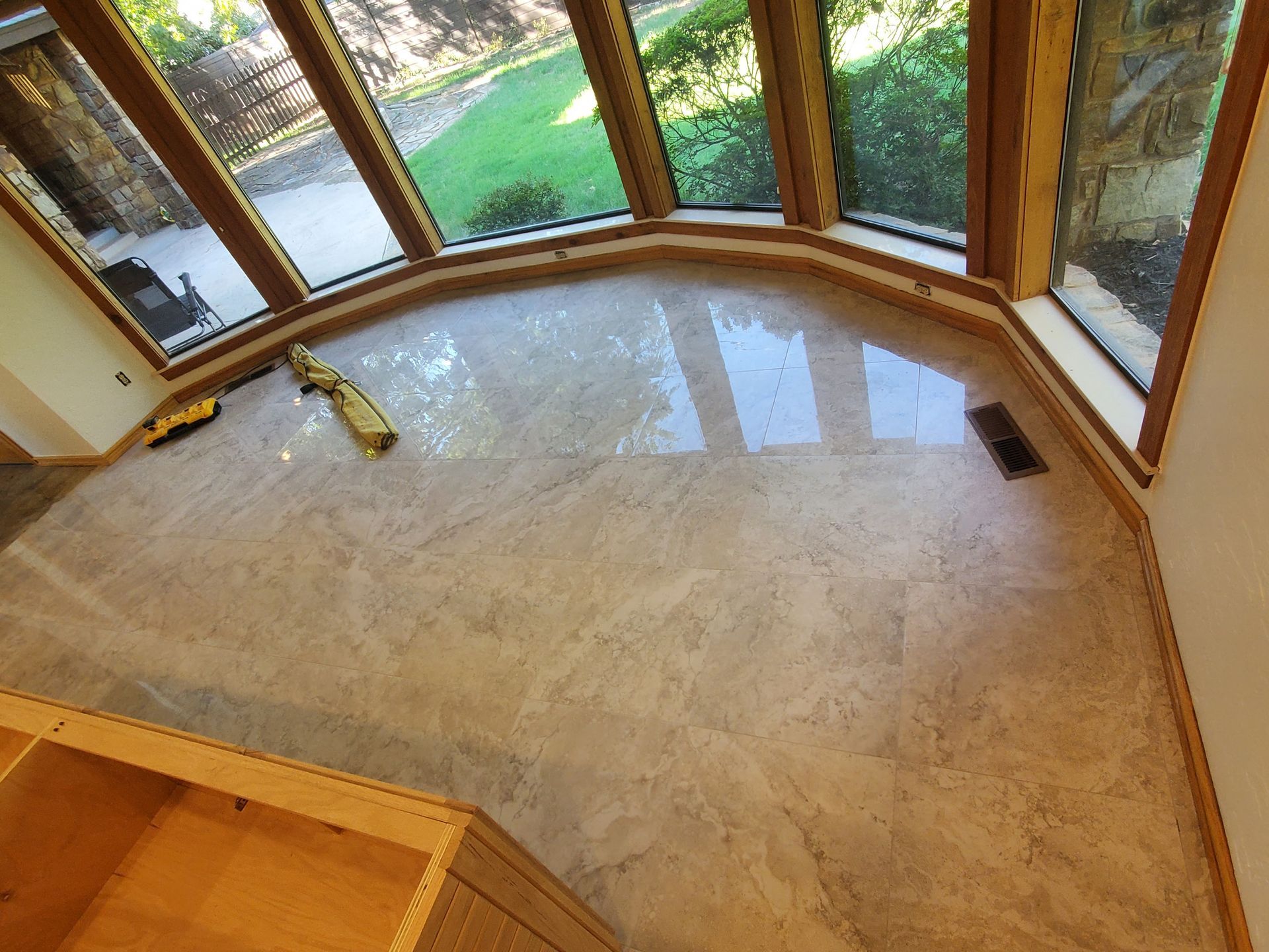 Empty sunroom with marble floor, wood-framed windows, and a cleaning bottle on the floor.