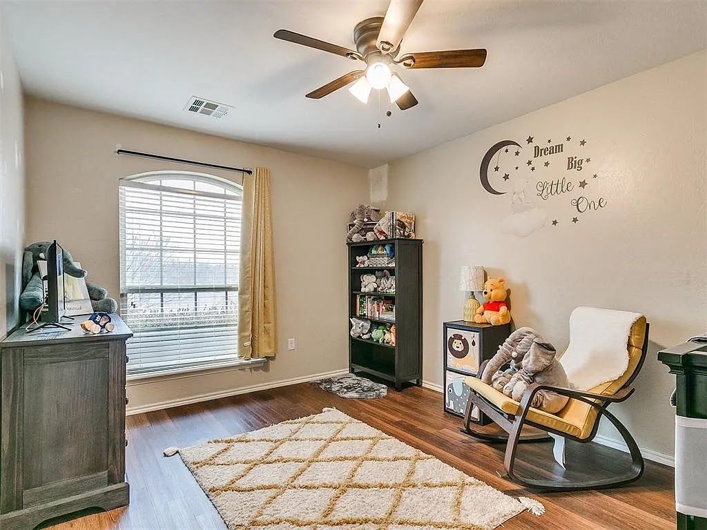 Bright nursery with crib, rocking chair, window blinds, ceiling fan, and wall decor.