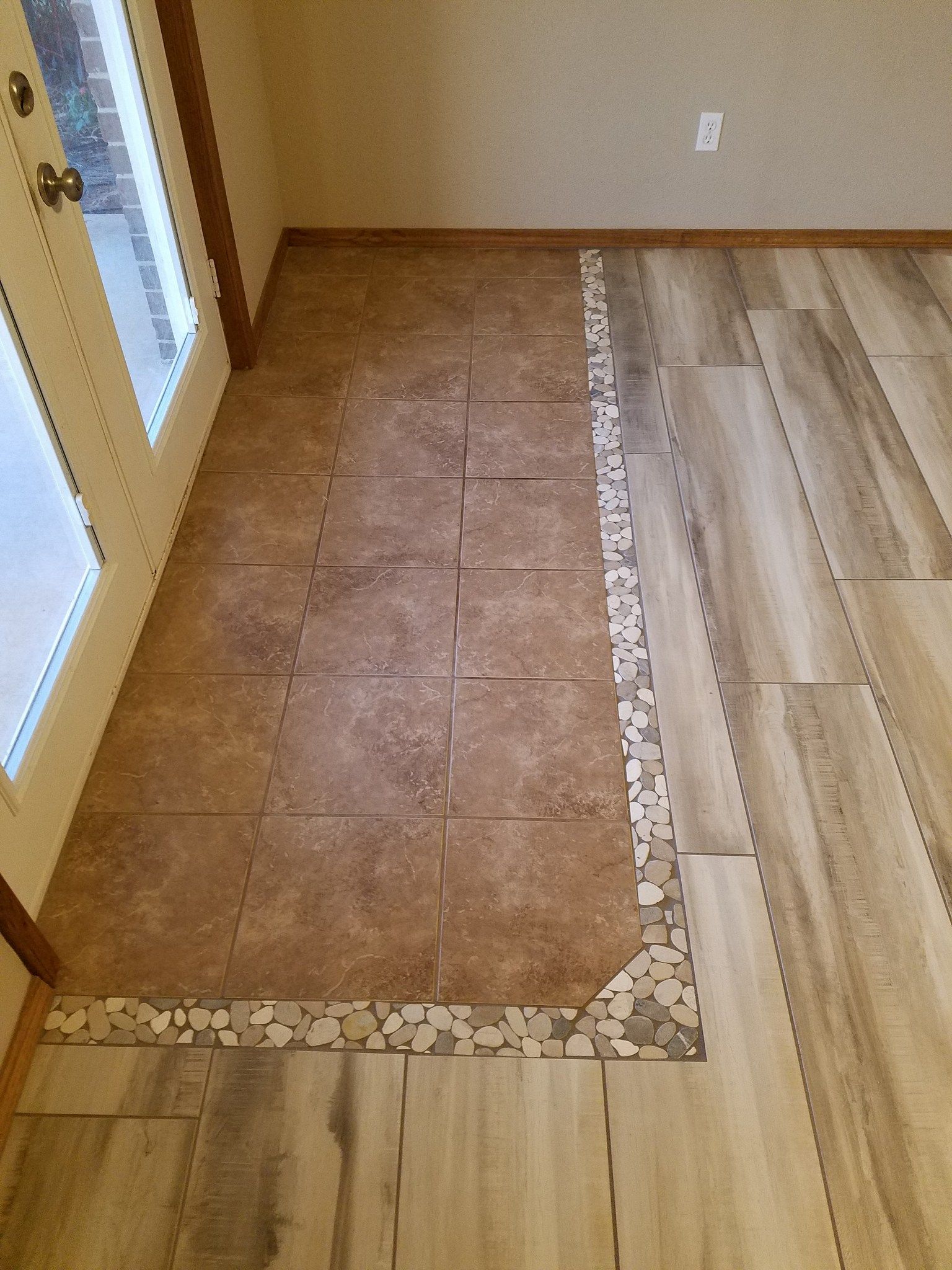 Partial tiled floor repair beside light wood flooring in a hallway corner
