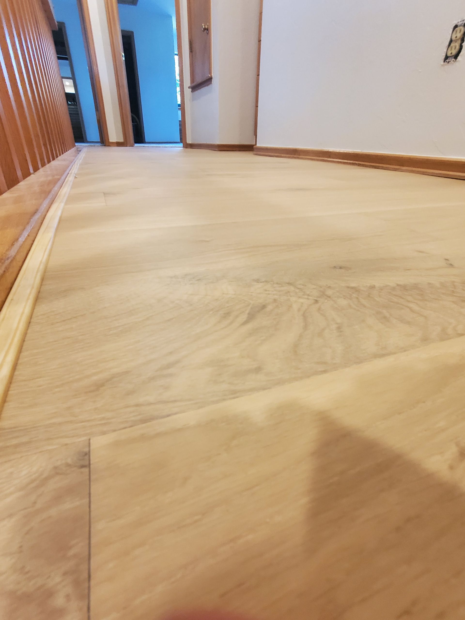 Wooden hallway floor with baseboards and open doorway at the end