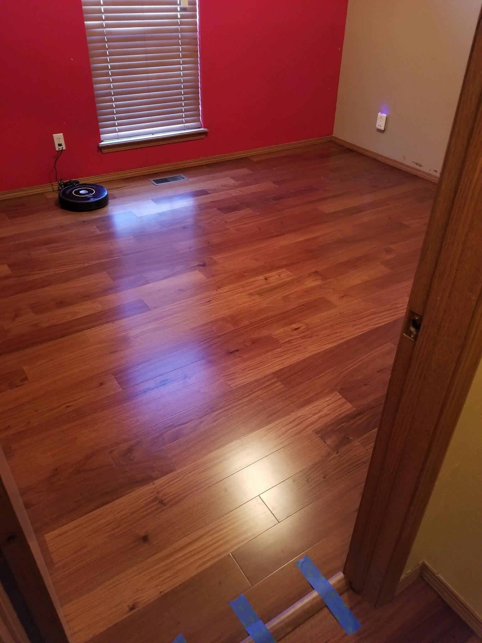 Empty room with hardwood floor, red walls, a window, and a taped marker on the floor.