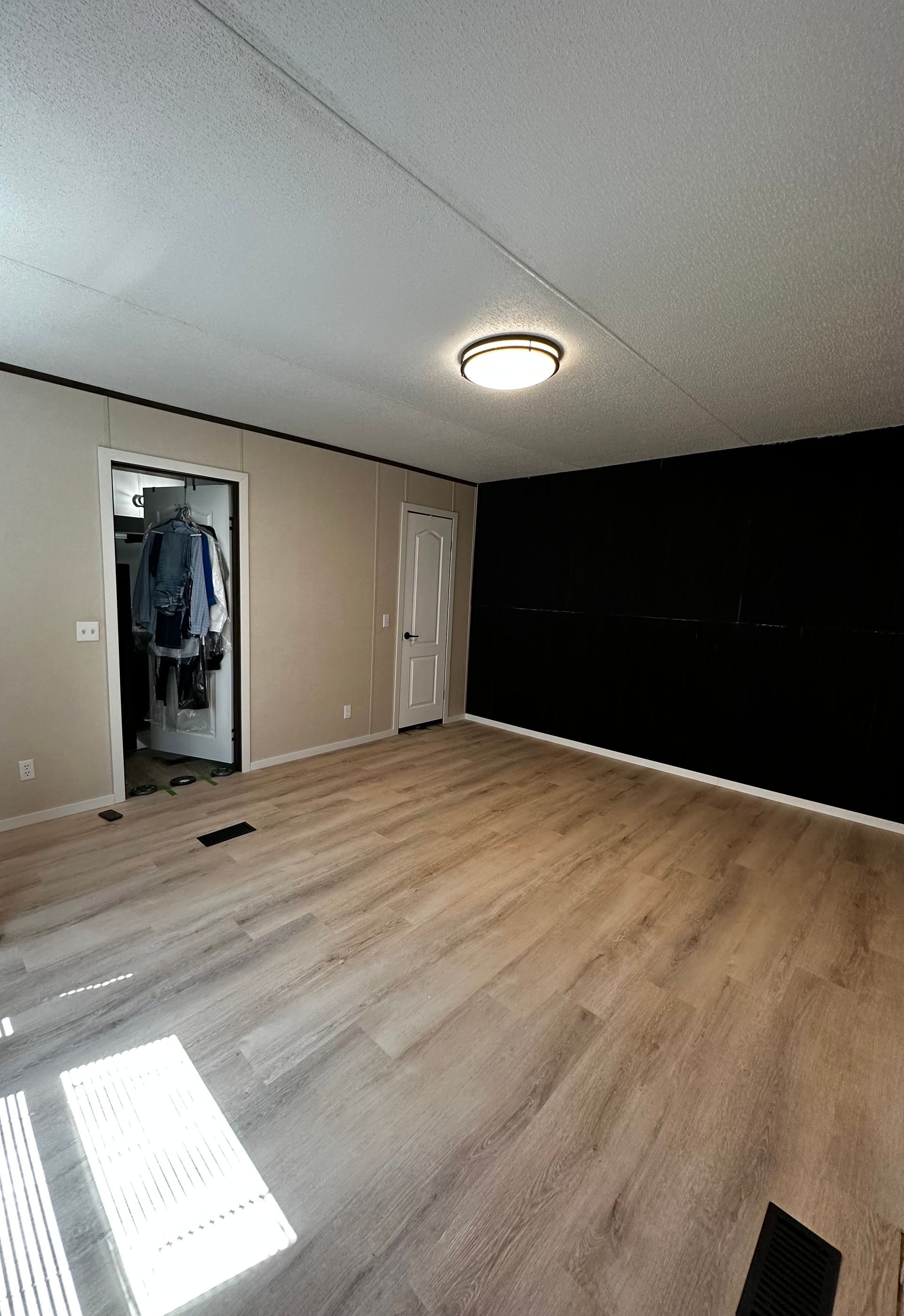 Empty room with light wood flooring, white ceiling, and a dark accent wall.