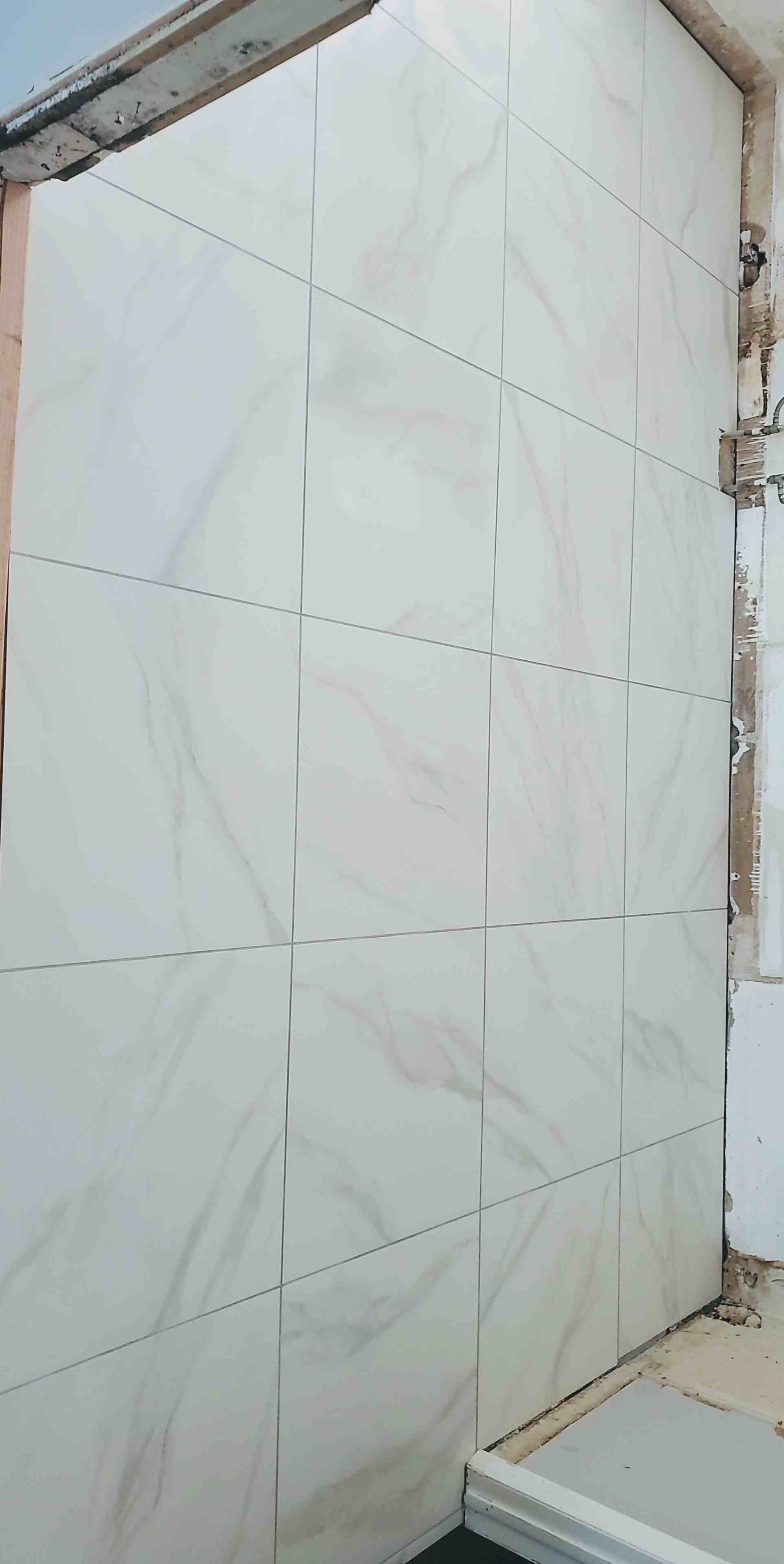White tiled wall or shower corner with marble-pattern tiles and exposed brick edges.