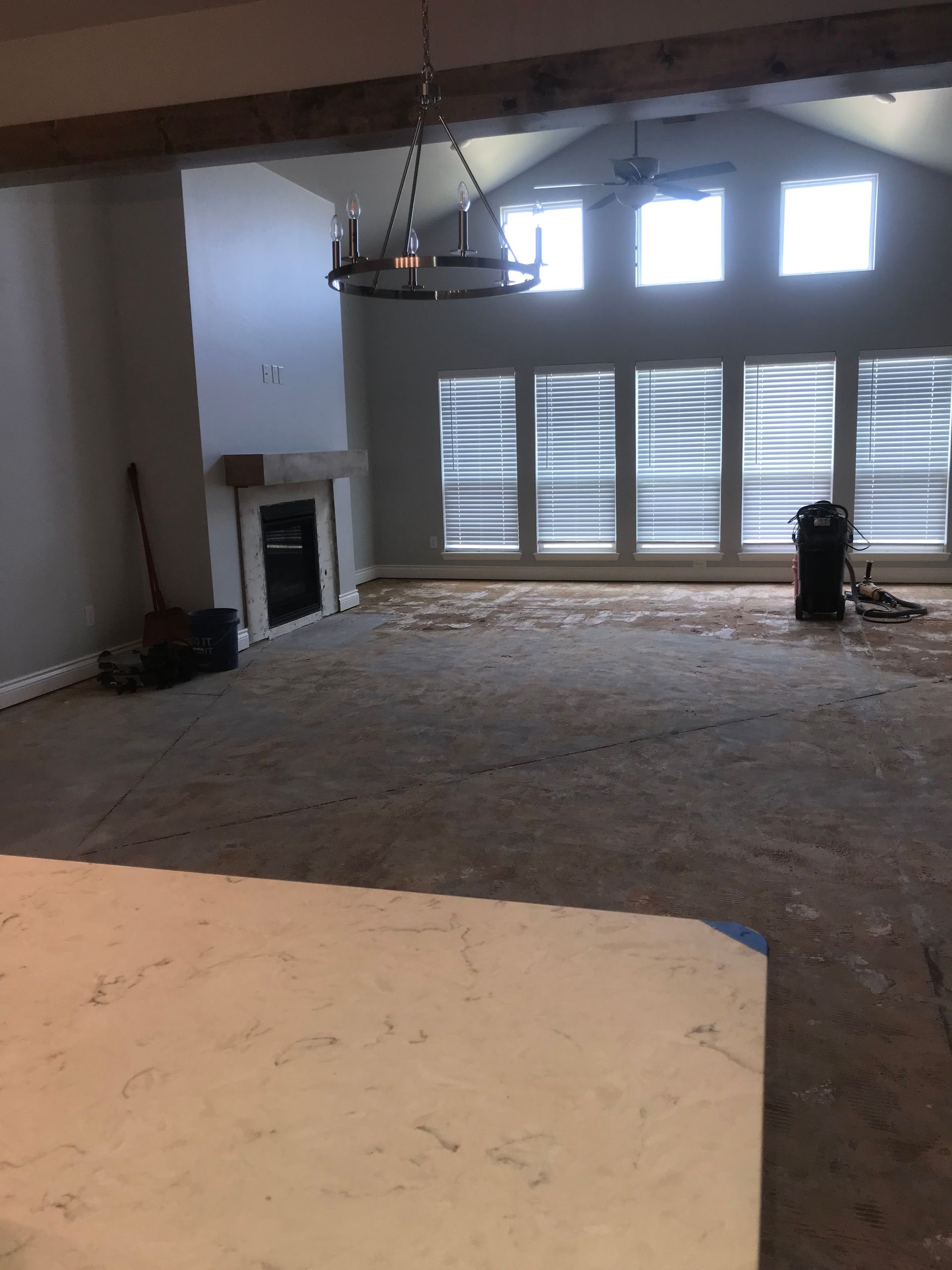 Empty living room with fireplace, ceiling fan, shuttered windows, and carpet removal in progress