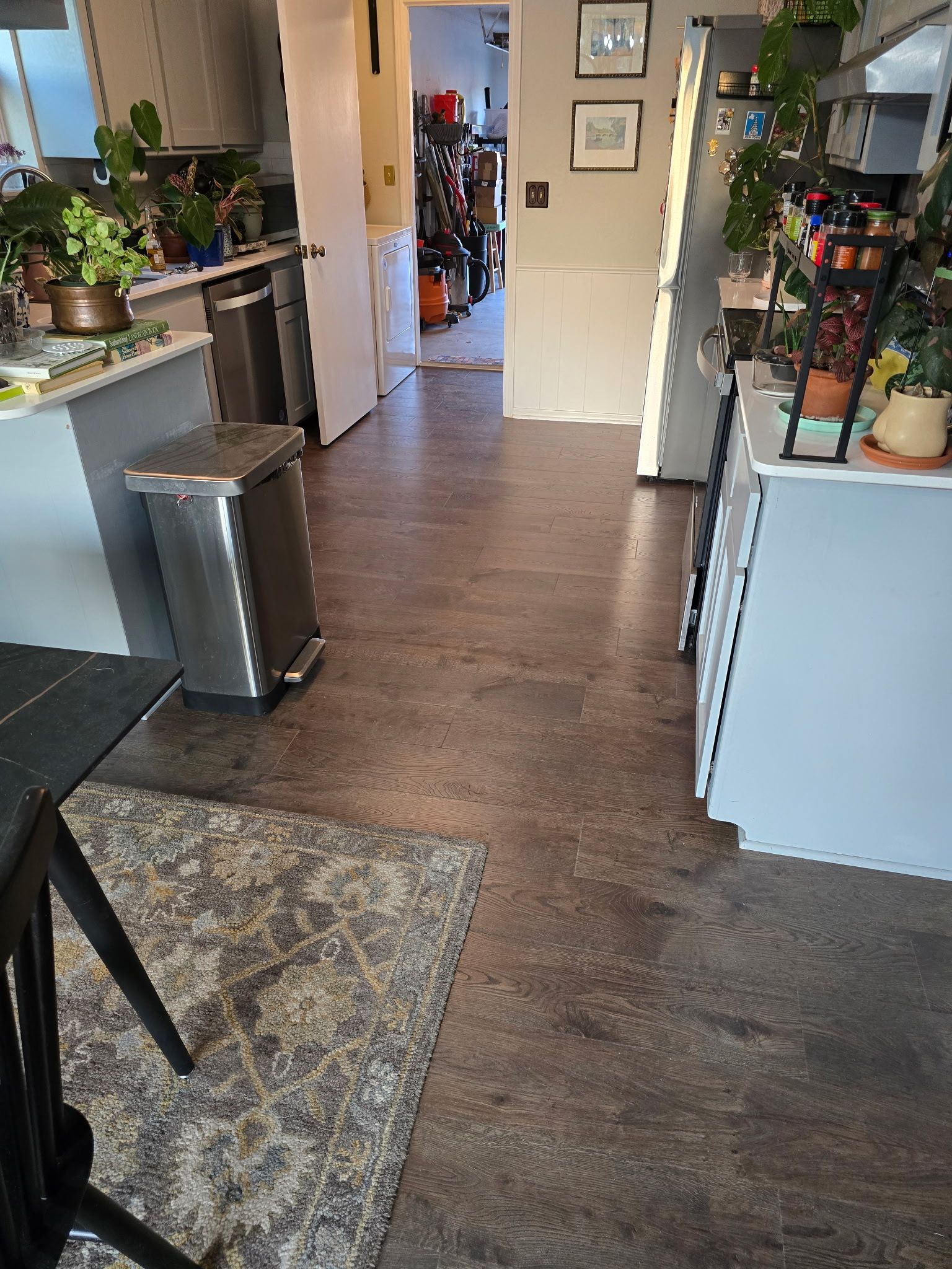 Bright indoor hallway with wood floors, potted plants, and a kitchen area on both sides