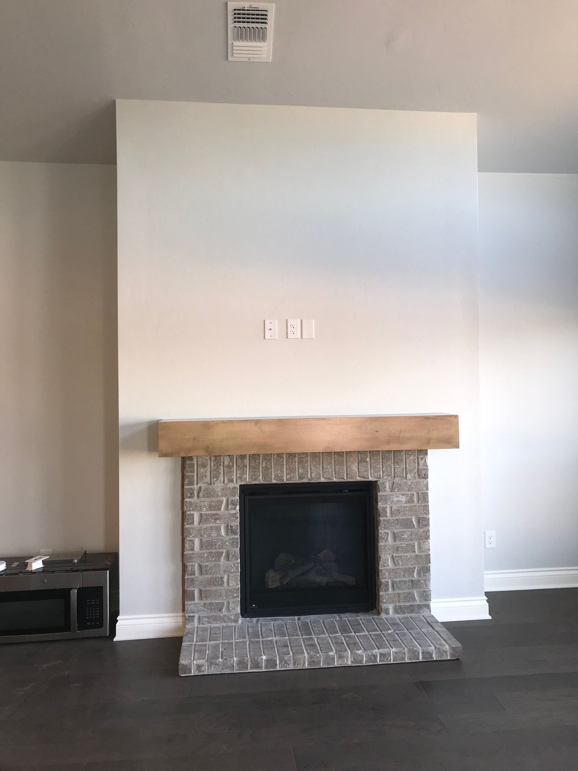 Living room fireplace with brick surround, wooden mantel, and a white wall above it.