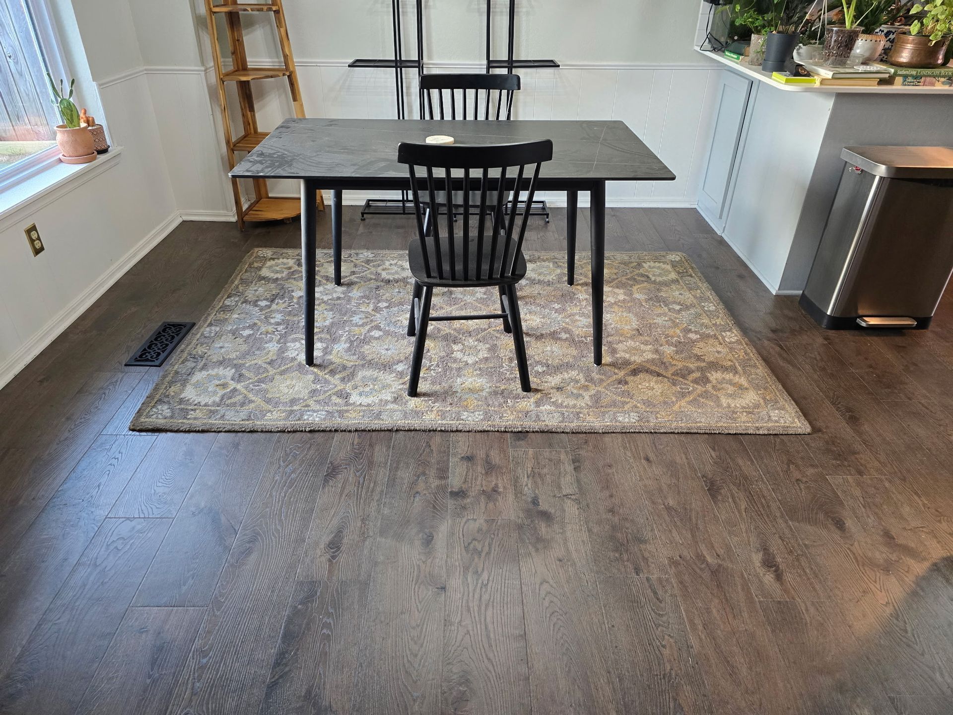 Dining area with black table and chair on a rug over wood flooring, beside a kitchen counter.