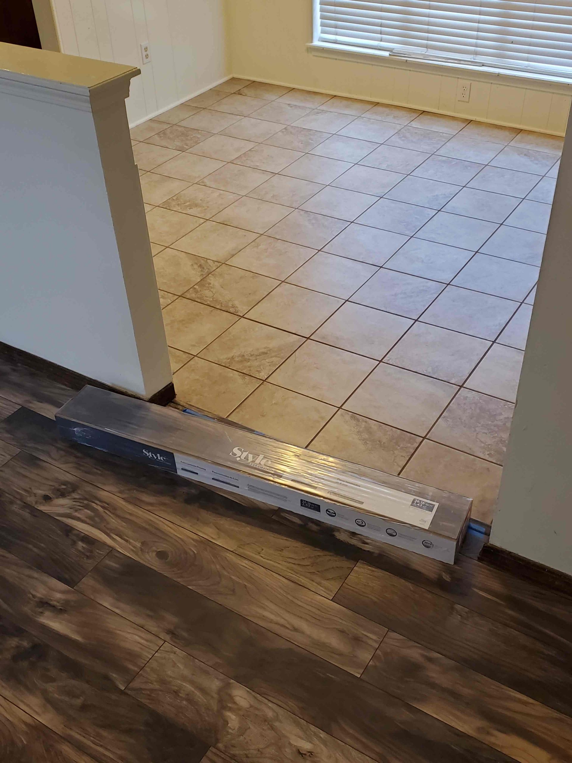 Threshold between wood floor and tiled room, with a long aluminum transition strip laid across it.